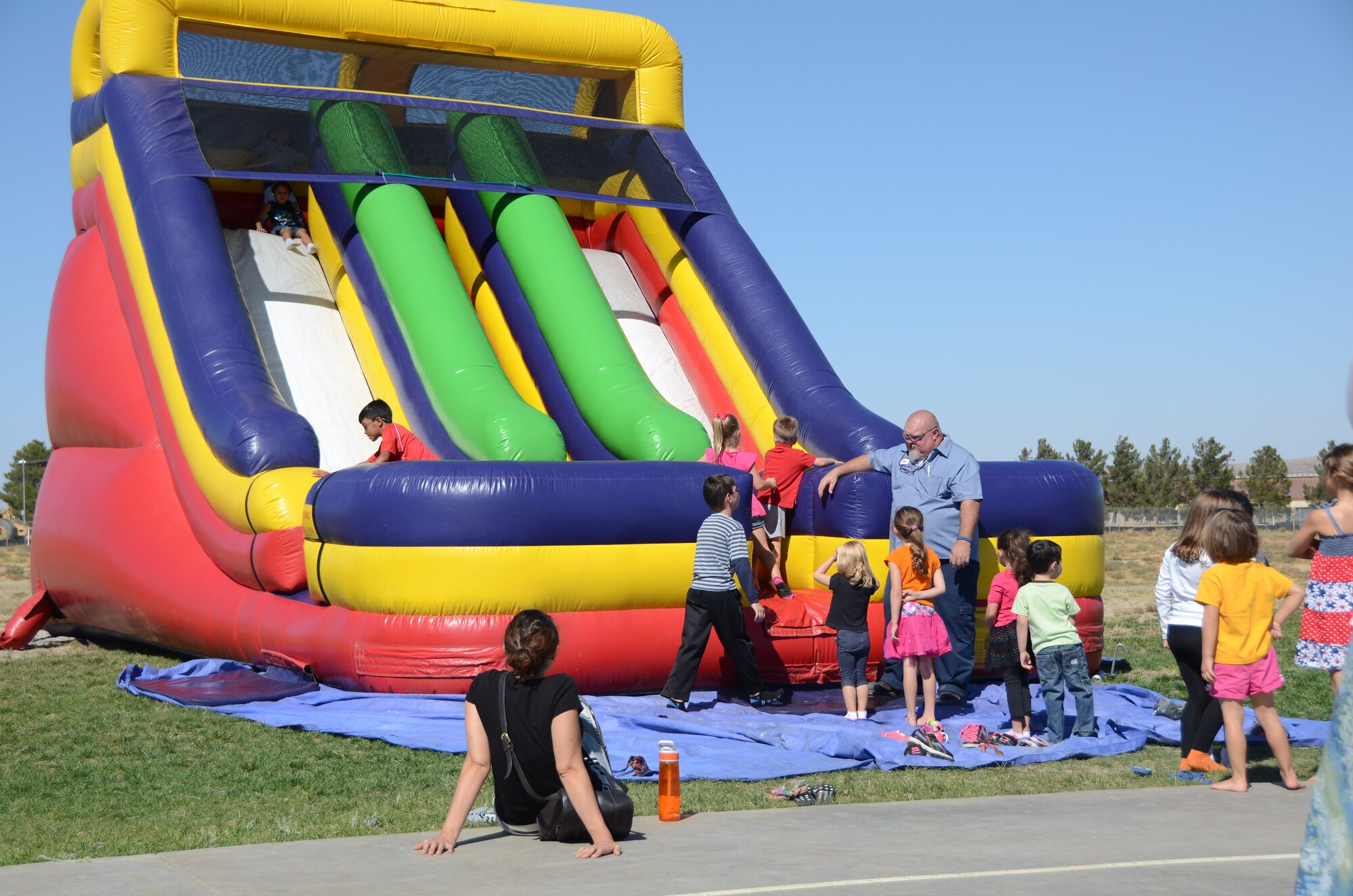 Corvias maintenance team member Robert West (standing) interacts with military children as they wait their turn on an inflatable slide at the 2014 Fallapalooza. The fall-themed event was sponsored by Corvias Military Living at Community Park on Saturday, October 18. (Courtesy phtoto by Mark Nettles)