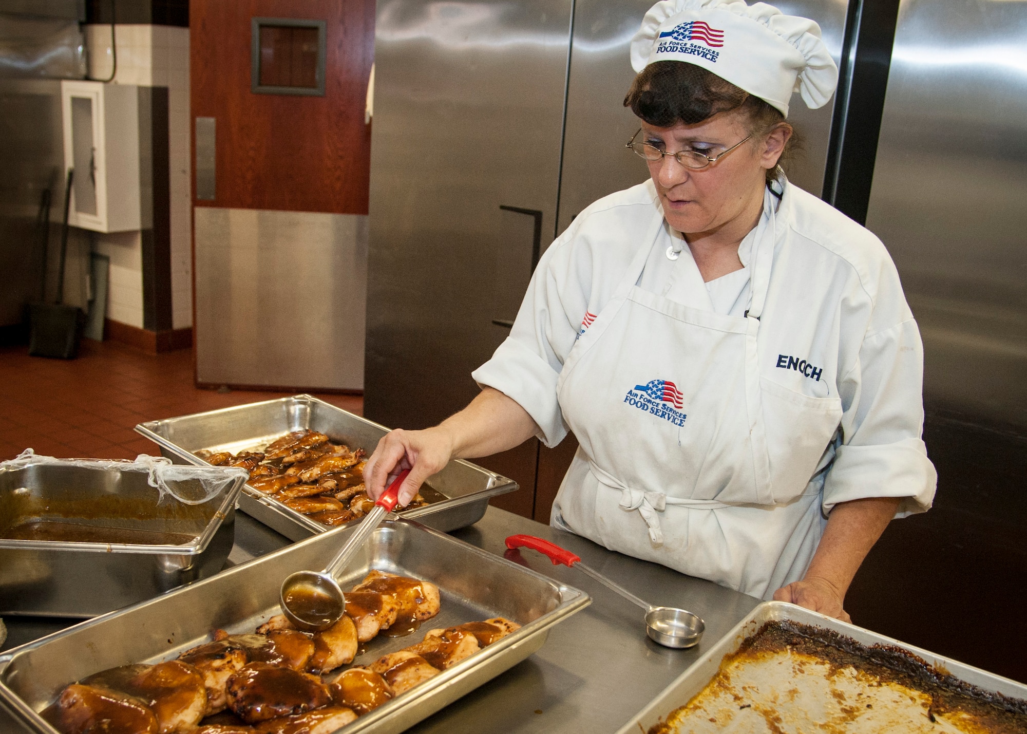 PETERSON AIR FORCE BASE, Colo. – Beverly Enoch, 21st Force Support Squadron civilian cook, pours a glaze over chicken breast in preparation for the day’s lunch service at the Aragon base dining facility Oct 16. Enoch, who has served at the Peterson DFAC for nearly 20 years, is part of a close-knit team comprised of active-duty Airmen and civilians who provide daily meals for the members of Team Pete. (U.S. Air Force photo/Staff Sgt. J. Aaron Breeden)