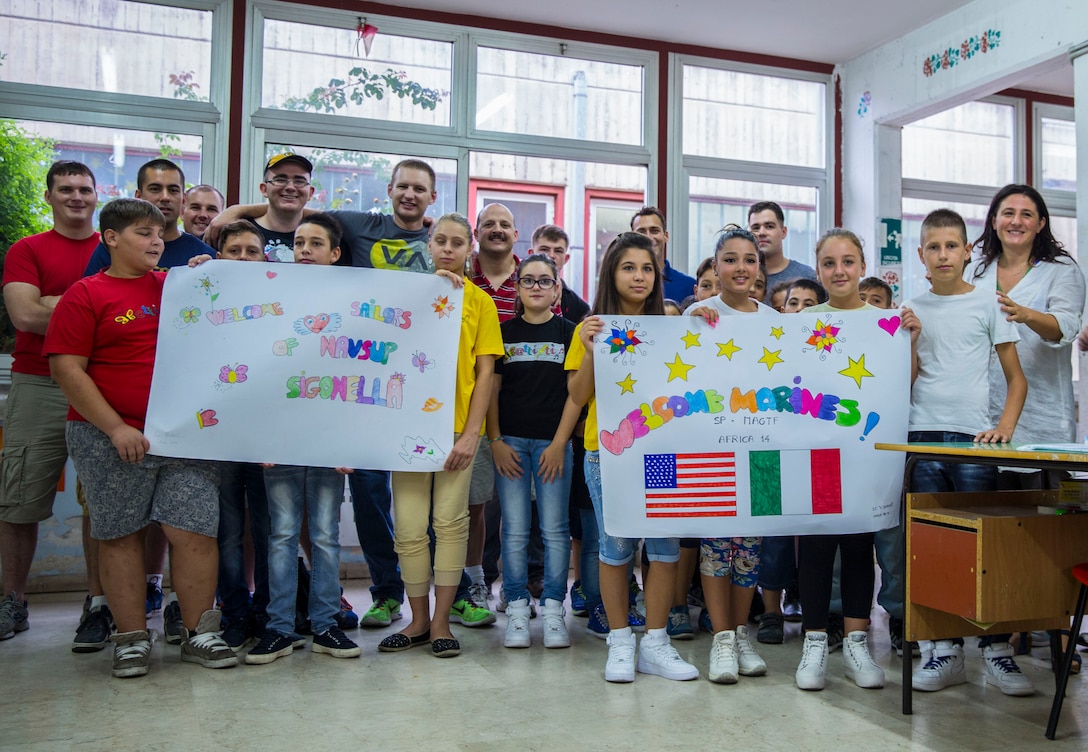 Service members of Special-Purpose Marine Air-Ground Task Force Africa 14 and Navy Supply pose for a photo with students during a community relations event at a local elementary school, the Istituto Comprensivo Cesare Battisti of Catania, in the San Cristoforo neighborhood, Sept. 25, 2014. During the event service members with SP-MAGTF Africa read to the students, donated books, told them about themselves and got to know the individual children while the Sailors of NAVSUP did a general cleanup of the school grounds. (U.S. Marine Corps photo by Cpl. Shawn Valosin)