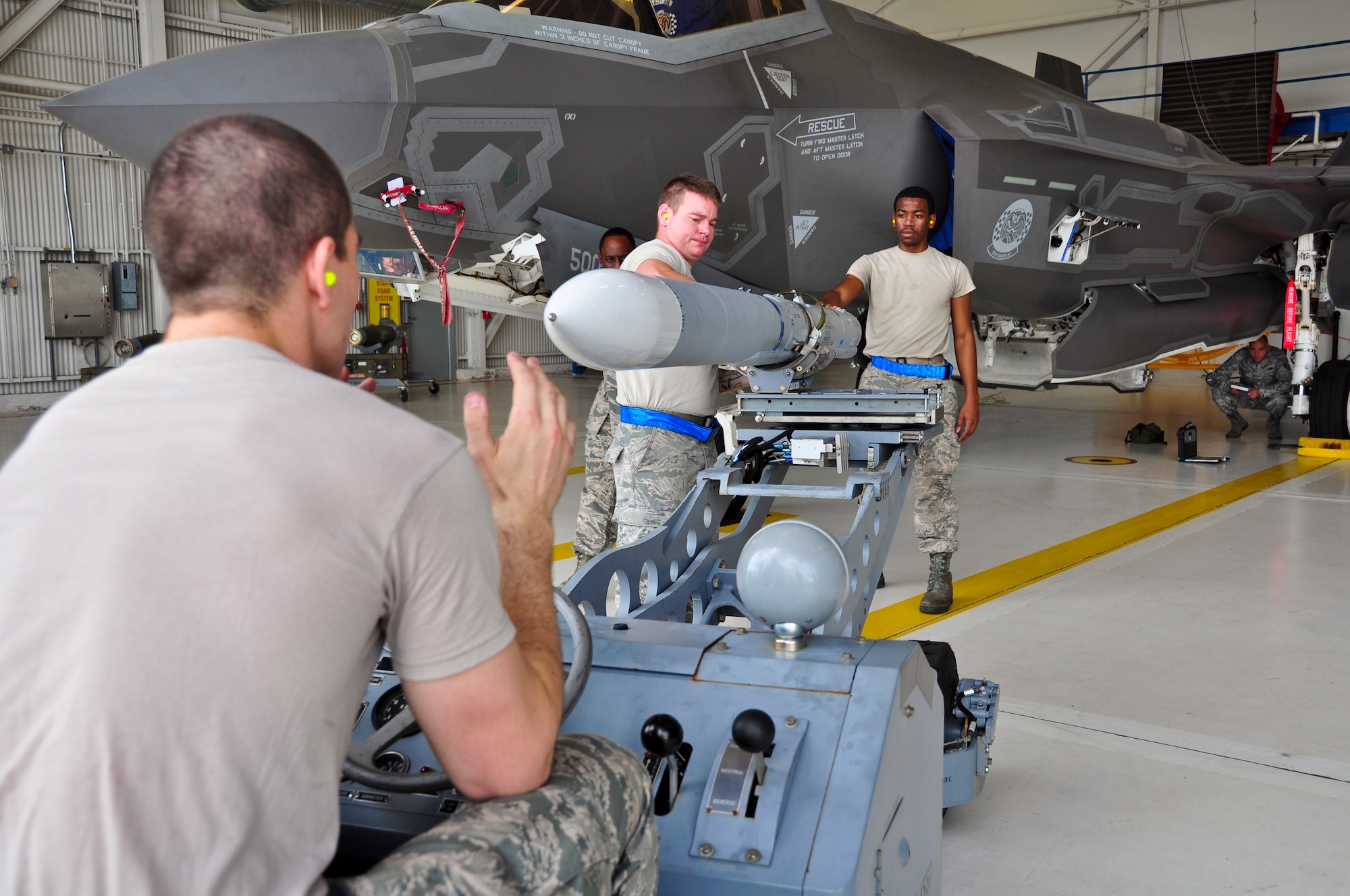 Airman 1st Class Reece Zoller, left, operates an MJ-1 lift truck carrying an AIM-120 advanced medium-range air-to-air missile as Staff Sgt. Zachary Watts, center, and Airman 1st Class Robert Hughes, right, guide him during a qualification load Oct. 10, 2014, at Eglin Air Force Base, Fla. The F-35 training program at Eglin AFB currently serves as the primary source of F-35 expertise to new F-35A units across the Air Force. Zoller, Watts and Hughes are load crewmembers from the 58th Aircraft Maintenance Unit crew one. (U.S. Air Force photo/Staff Sgt. Marleah Robertson)