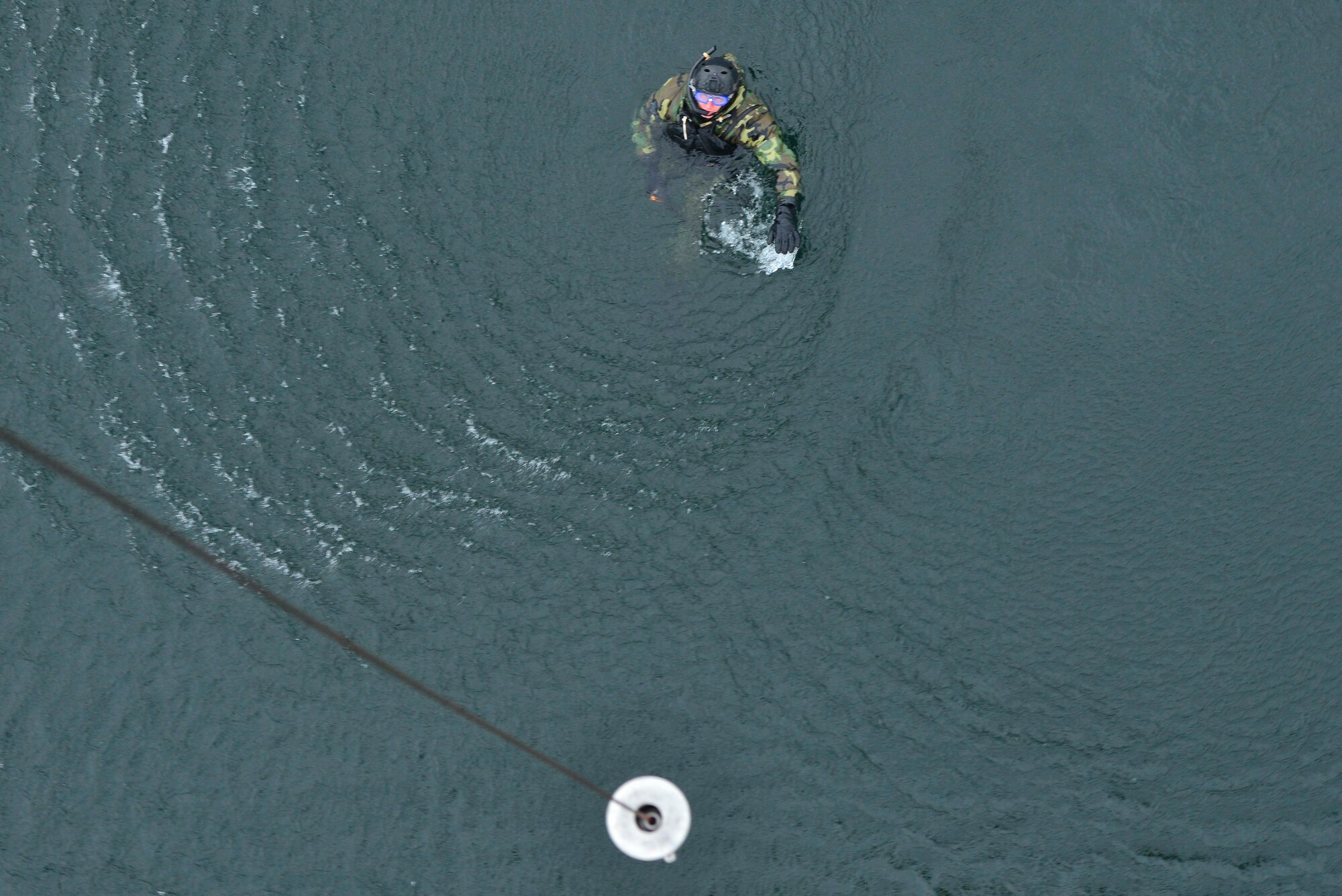 Capt. Matthew Arnold swims towards a hoist from a UH-1N Iroquois helicopter during a water operations training scenario Oct. 17, 2014, at Long Lake, Washington. As part of the water operations training, Arnold entered the water, waited for the pilot to make several passes to familiarize themselves on approach and hoisting procedures over water. Once in the water and actions were complete, swimmers would communicate to the pilots that they were ready for pick-up using hand signals over their heads.  The flight engineer would then hoist the swimmers up from approximately 40 feet.  Some pilots were tasked to complete several attempts of ‘helo-casting’ and hoisting to complete their search and rescue certification while others were trainers or used the mission as re-certification. (U.S. Air Force photo/Staff Sgt. Alexandre Montes)