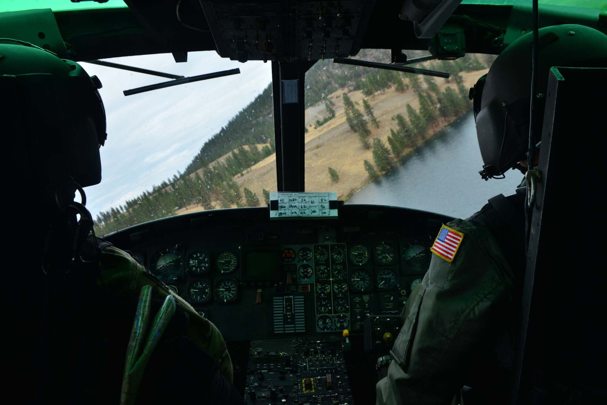 Maj. Dee Bochte and Capt. Josiah Hart, 36th Rescue Flight helicopter pilots, look for safe landing zone for freefall swimmers from the 336th Training Group during a water operations training scenario Oct. 17, 2014, at Long Lake, Washington. The training was held to train new helicopter pilots and aircrew assigned to the 36th Rescue Flight with maneuvering and retracting persons from water situations. On average, the unit responds from 15 to 20 emergencies each year and is credited with saving more than 687 lives since its inception in 1971. These missions included search and rescue for crashed aircraft and lost hikers, fisherman and hunters; notification and evacuation of backcountry personnel in the face of Washington's worst fire season in seven years; transport of a critically-injured gunshot victim; and the rescue of a seriously injured back-country snowboarder with a 200-foot hoist using night vision in Sandpoint, Idaho. (U.S. Air Force photo/Staff Sgt. Alexandre Montes)