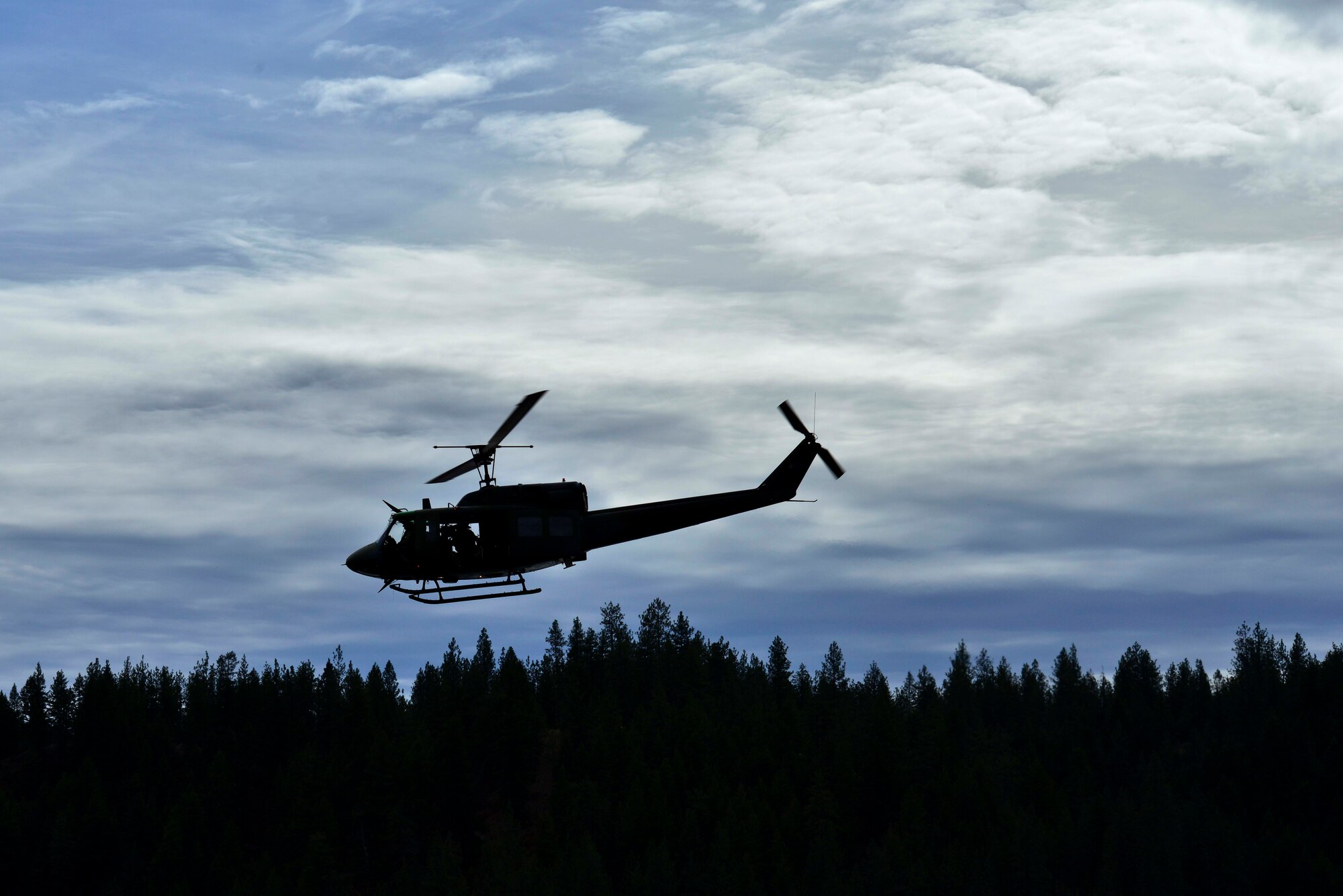 A UH-1N Iroquois helicopter from the 36th Rescue Flight passes over a tree line while looking for a safe potential water landing zone for 336th Training Group combat rescue officers to practice their freefall swimmer deployment during a water operations training scenario Oct. 17, 2014, at Long Lake, Washington. The 36th RQF supports the 336th TRG through hands-on helicopter operations for more than 3,000 students per year. Training is conducted year-round at Fairchild and at the school's field location in the Colville National Forest, about 60 miles north of the base. Flight operations include live rescue hoist training, para drop demonstrations, and combat rescue procedures training for students in the basic Combat Survival Course. (U.S. Air Force photo/Staff Sgt. Alexandre Montes)