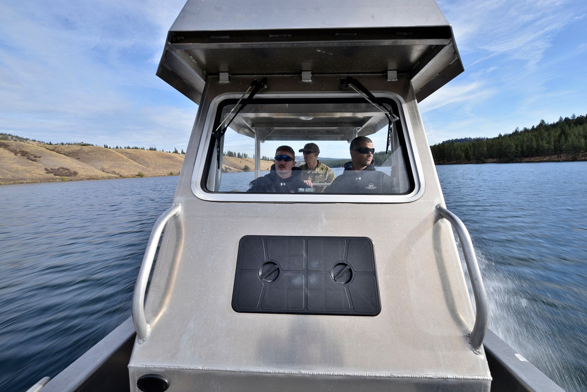 Airman 1st Class Gene Sauder, 336th Training Support Squadron aircrew flight equipment, Staff Sgt. Gary Roland, 66th Training Squadron water survival instructor and Senior Airman Justin Mason, 336th TRSS AFE, drive a boat along the lake looking for a safe landing zone for combat rescue officers during water operations training Oct. 17, 2014, at Long Lake, Washington. Water operations training helps combat rescue officers simulate response to isolated personnel in several water situations.  The watercraft crew comprised support personnel such as independent duty medical technicians, a safety diver and AFE airmen in case of an emergency.  (U.S. Air Force photo/Staff Sgt. Alexandre Montes) 