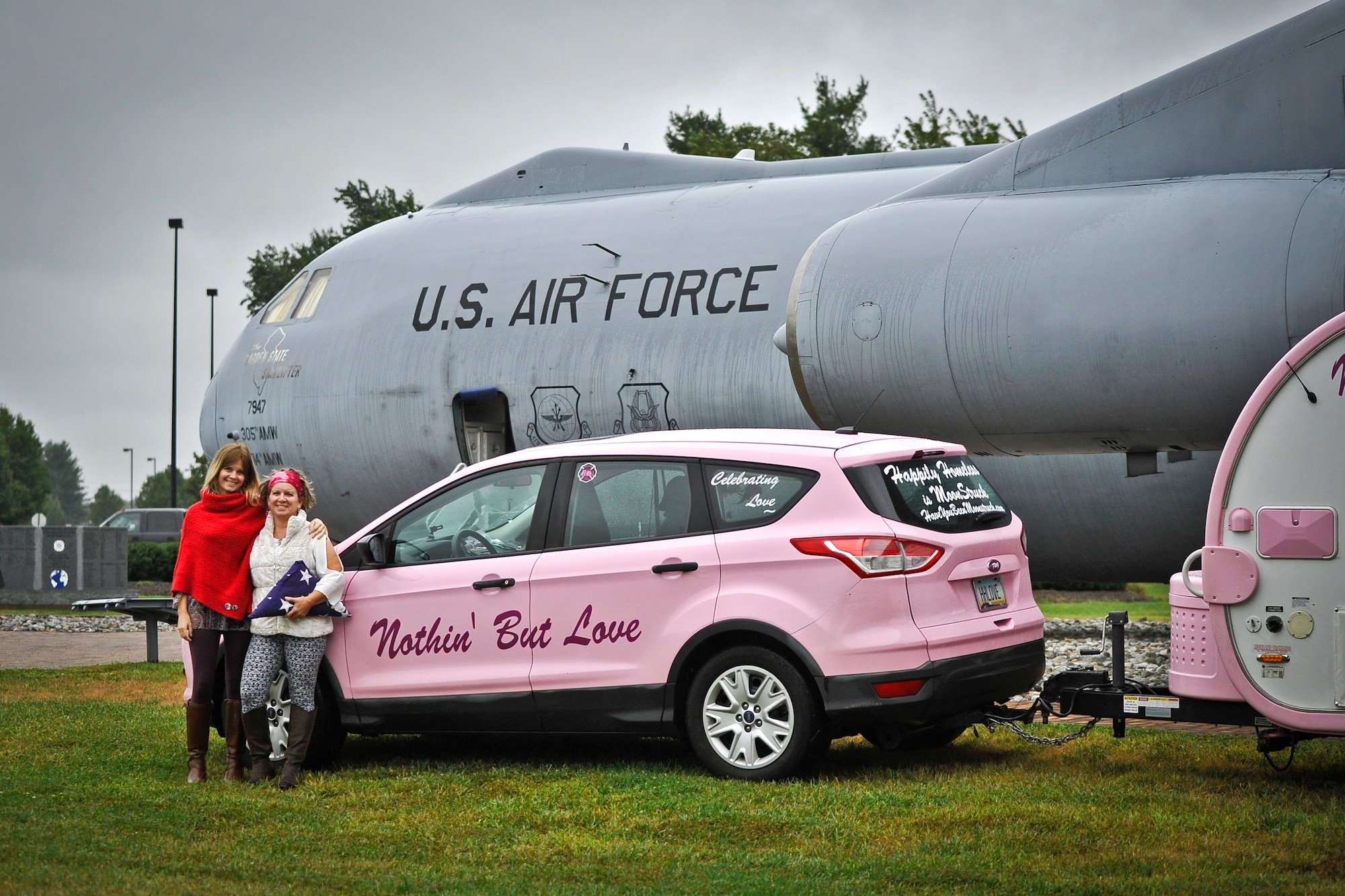 Rachael-Grace Aganda and her mother, Alison Miller, pose in front of their vehicle, which is in front of a static C-141B Starlifter aircraft Sept. 29, 2014, at Joint Base McGuire-Dix-Lakehurst, N.J. Miller, widow of retired Air Force Master Sgt. Chuck Dearing, and Aganda, daughter of Dearing, embarked on a journey to travel across the U.S. in a custom painted SUV and trailer to celebrate a late husband and father’s life on what they call an “Odyssey of Love”. The significance of posing in front of the C-141 is that Dearing worked on the aircraft before retiring from active duty. (U.S. Air Force photo by Staff Sgt. Scott Saldukas/Released)