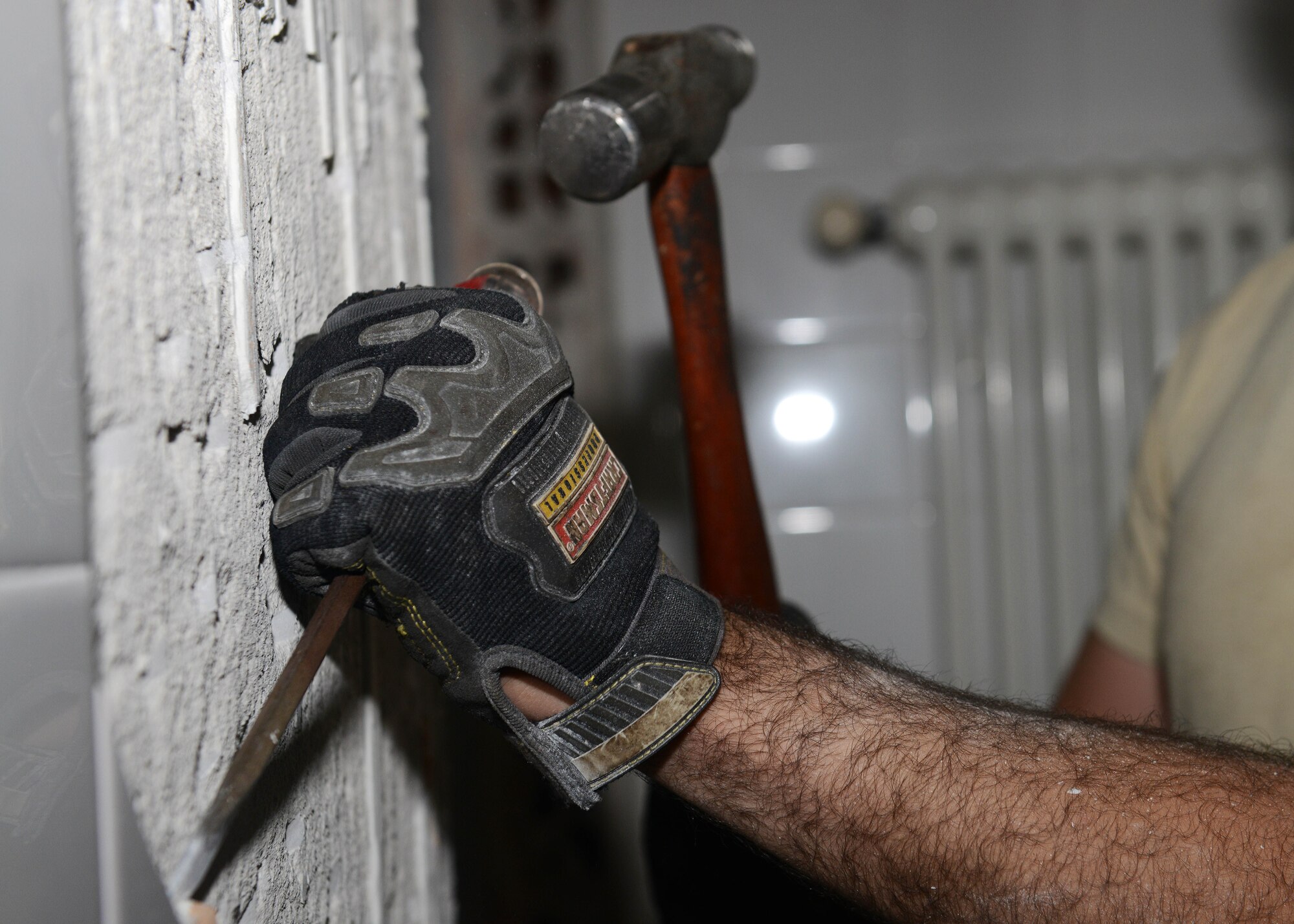 Senior Airman Nicholas Perry, 31st Civil Engineer Squadron structures journeyman, hammers off reusable tiles, Oct. 20, 2014, at Aviano Air Base, Italy. The salvaged tiles will be reused for the Troop Training Project that will convert an empty building into the new urinalysis testing facility. (U.S. Air Force photo/Airman 1st Class Deana Heitzman)
