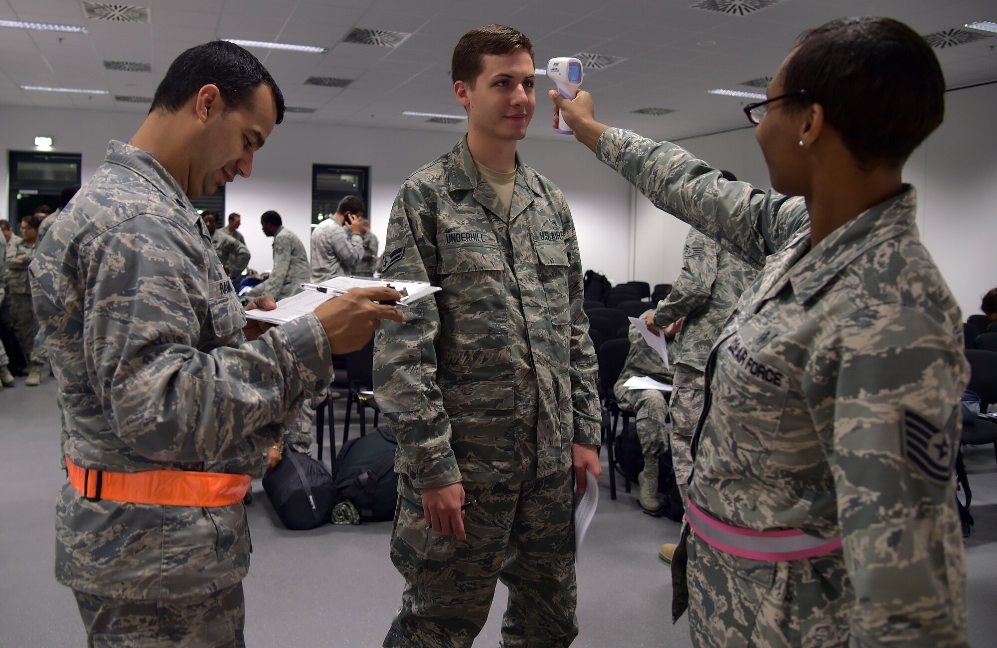 Airman 1st Class Mark Underhill (middle), 633rd Medical Group medical technician has his temperature taken by Tech. Sgt. Saquadrea Crosby(right), 86th AMDS public health NCOIC as Lt. Col. Juan Ramirez (left), 86th Aerospace Medicine Squadron public health flight commander, logs the information at a passenger holding facility at Ramstein Air Base, Germany, Oct. 19, 2014. Any personnel traveling into Ramstein from Ebola infected areas will be medically screened upon their arrival and cleared by public health for onward travel to ensure the health and safety of all passengers, aircrew and members of the Kaiserslautern community. (U.S. Air Force photo/Staff Sgt. Sara Keller)