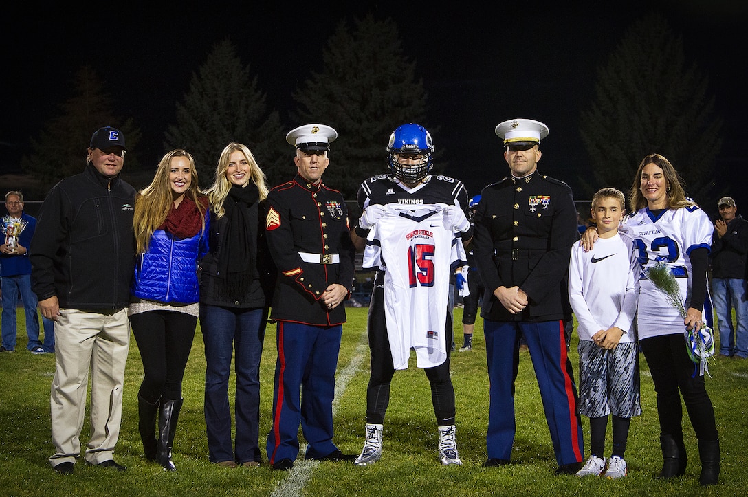Drew Berger (center), an inside linebacker for the Coeur d’Alene High School Vikings and 17-year-old native of Coeur d’Alene, Idaho, stands alongside his family and receives his Semper Fidelis All-American Bowl jersey from Sgt. Alex Angle (left), a local Marine recruiter, and Capt. Ryan Sahlberg (right), the operations officer of Marine Corps Recruiting Station Seattle, before a game against the Lake City High School Timberwolves at Coeur d’Alene High School in Coeur d’Alene, Oct. 17, 2014. Berger is the sole Idaho player among approximately 100 student athletes from across the nation selected to participate in the game at the StubHub Center in Carson, Calif., Jan. 4, 2015. He follows in the footsteps of his brother Chase Blakley, a fellow Vikings football alum and Boise State University football player who played in last year’s Semper Fidelis All-American Bowl. (U.S. Marine Corps photo by Sgt. Reece Lodder)