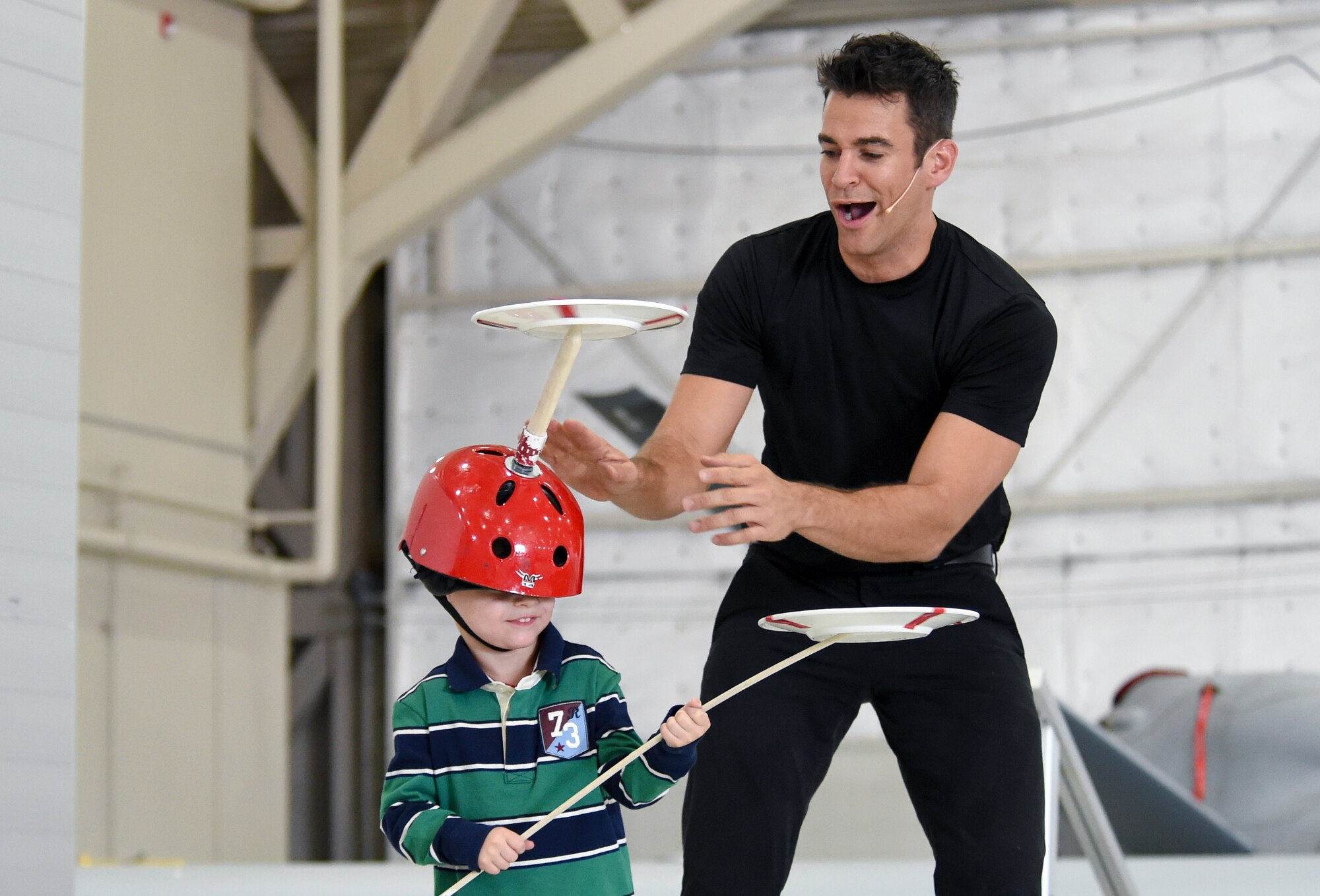 Andrew Kearce, son of Tech. Sgt. Dustin Martinez, 432nd Aircraft Maintenance Squadron specialist section chief, helps entertainer, Jeff Civillico, balance plates during a performance at Creech Air Force Base, Nevada, Oct. 17, 2014. Civillico performed a juggling and comedy routine for base members and their families as part of a new Freedom Friday Concert Series the USO is sponsoring at Creech. (U.S. Air Force photo by Tech. Sgt. Shad Eidson/Released)