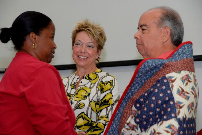 Egidia Bell, Quilts of Valor Foundation area representative, presents retired Air Force Lt. Col. Allison Farley and his wife Audrey, a Quilt of Valor, Oct. 23, 2014, at the Naval Consolidated Brig Charleston on Joint Base Charleston, S.C. Quilts of Valor’s mission is to cover all service members and veterans touched by war with comforting and healing quilts. Farley was at NCBC to receive his new companion dog, Mordecai. (U.S. Air Force photo/Eric Sesit)