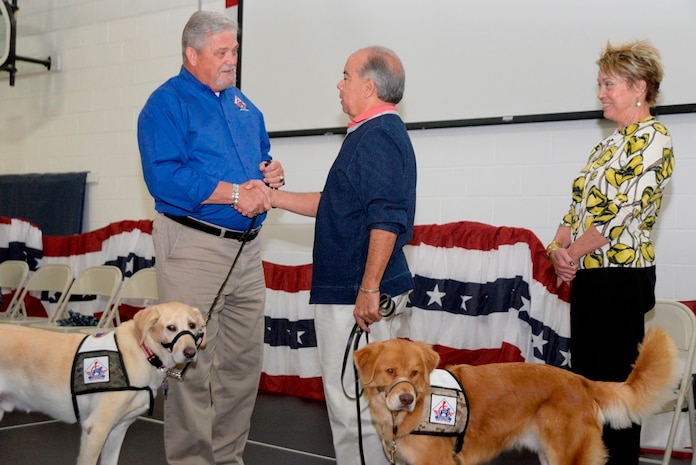 Rick Hairston, co-founder of Carolina Canines for Service and his dog Titus (left), present retired Air Force Lt. Col. Allison Farley with his new service dog Mordecai, a two-year old Nova Scotia Duck Tolling Retriever as Farley’s wife Audrey looks on Oct. 23, 2014, at the Naval Consolidated Brig Charleston on Joint Base Charleston, S.C. Canines for Service is dedicated to empowering people with disabilities to achieve greater independence and enhanced quality of life and to improving people's lives through the services of specially trained assistance. The training of a Canines for Veterans service dog takes about one year. Rescue dogs are trained by military prisoners and will learn more than 90 commands including basic obedience, intermediate skills like retrieving items and advanced skills such as opening doors. (U.S. Air Force photo/Eric Sesit)