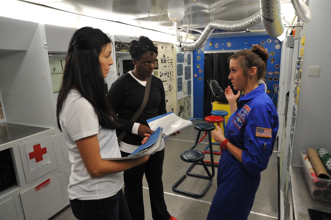 Space Camp Crew Trainer Hanna McCravy explains mission support actions to Amy Webb and Carla McNeal during the space shuttle mission portion of the U.S. Space & Rocket Center corporate camp. Webb and McNeal are members of the U.S. Army Engineering and Support Center, Huntsville's Leadership Development Program II. The shuttle mission provided participants with a close look at how a shuttle mission is executed and the  role each participant plays to accomplish the mission. LEadership and communications skills are realized during the mission as adversity is often added to the mission to provide realism. 