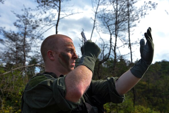 U.S. Air Force Senior Airman Andrew Spears, 5th Reconnaissance Squadron maintenance operations center controller, signals pilots with a mirror to show his location during a combat search and rescue training scenario at an off base training site, Republic of Korea, Oct. 14, 2014. The training was conducted to better prepare the Airmen involved to locate and recover isolated personnel in remote areas with different terrain. (U.S. Air Force photo by Senior Airman David Owsianka/Released)