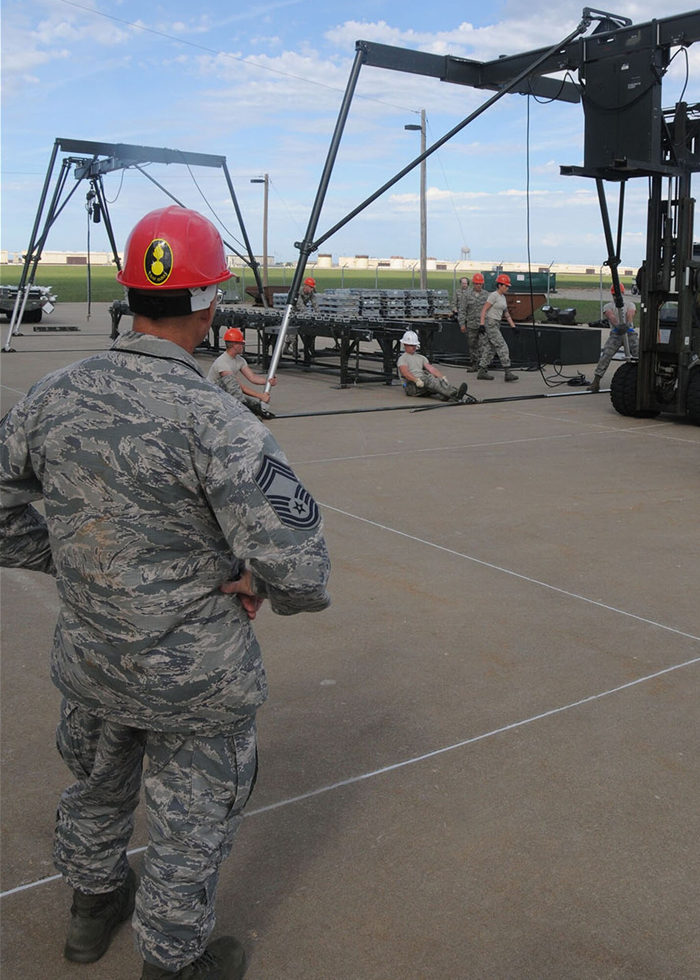 Chief Master Sgt. Erick Hays, one of the Global Strike Command evaluators, watches on as Airmen from the Whiteman Air Force Base munitions squadron construct a munitions assembly conveyor as part of the October 2014 Global Strike Challenge.  The Global Strike Challenge is designed to promote esprit de corps, recognize the Air Force’s outstanding Global Strike personnel and teams, and to improve capabilities through competition. (U.S. Air National Guard photo by Senior Airman Nathan Dampf/RELEASED)