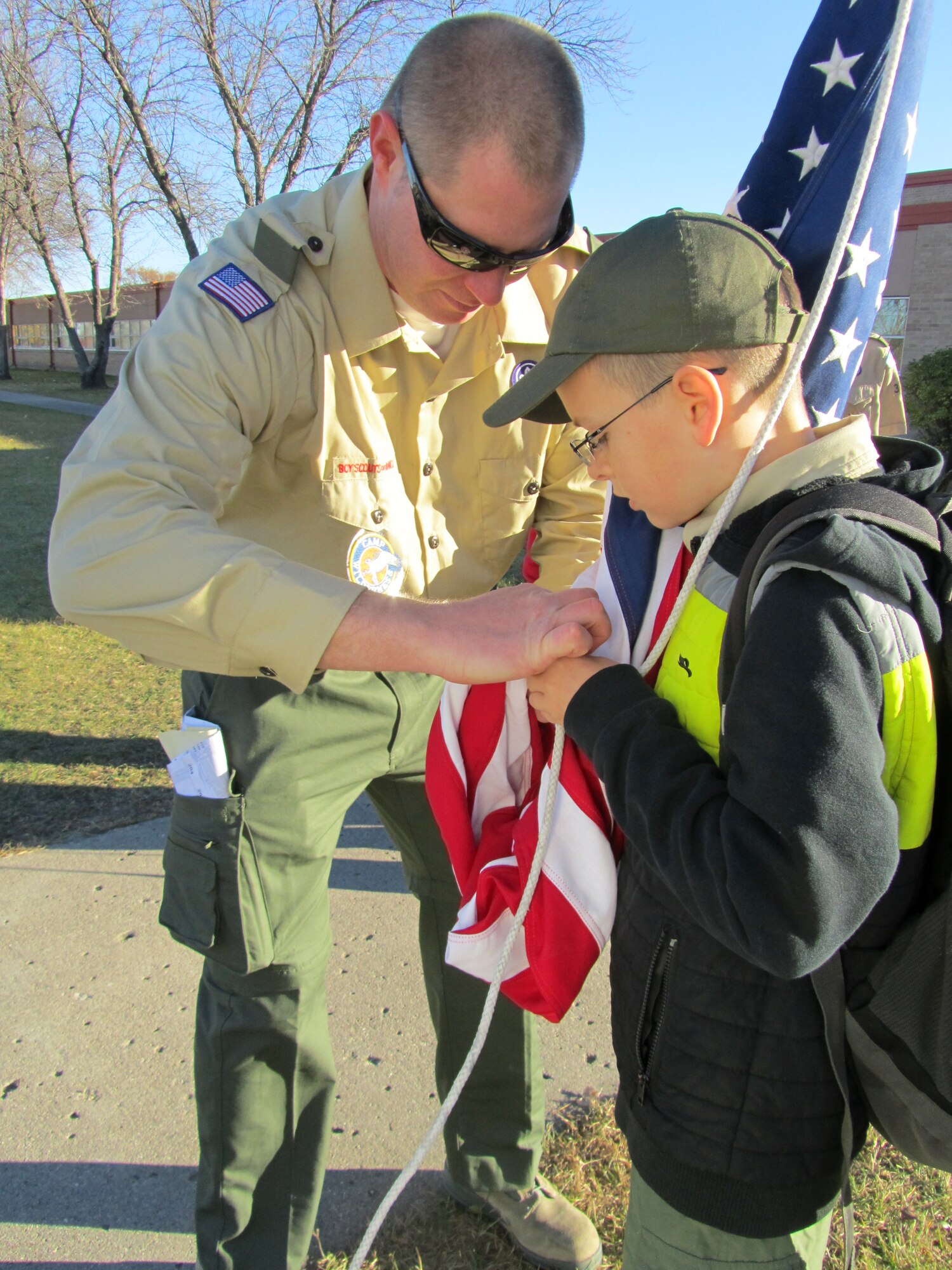 Master Sgt. Chris Miller, Grand Forks Air Force Base Boy Scout Troop 319 leader, helps Devyn Meneses attach the American flag to the lanyard during a flag detail at Twining Elementary and Middle School on Grand Forks Air Force Base, N.D., Oct. 25, 2014. The members of Boy Scout Troop 319 learned how to raise and lower the flag, as well as proper folding and carrying techniques. (Courtesy photo)