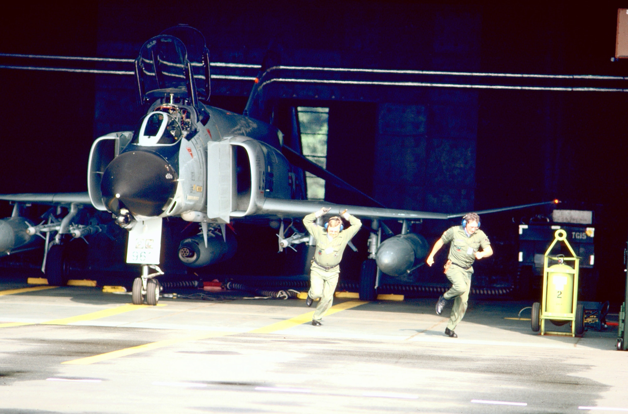 Crew members scramble out of the alert hangar past an ANG F-4D Phantom II aircraft about to launch on a mission during Creek Klaxon, a deployment where Air National Guard units from 20 states were sent to temporarily assume the Zulu Alert duties of the 526th Tactical Fighter Squadron (USAFE) at Ramstein Air Base, Germany, from 1 April 1986 to 1 April 1987. 