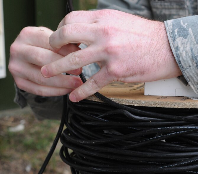 U.S. Air Force Senior Airman Christopher Cole, 100th Communication Squadron cyber transport technician from Merced, Calif., reels in a cable Sept. 17, 2014, on RAF Mildenhall, England. Cole set up a connection on the flightline so planes can connect to the network. (U.S. Air Force photo by Gina Randall/Released)