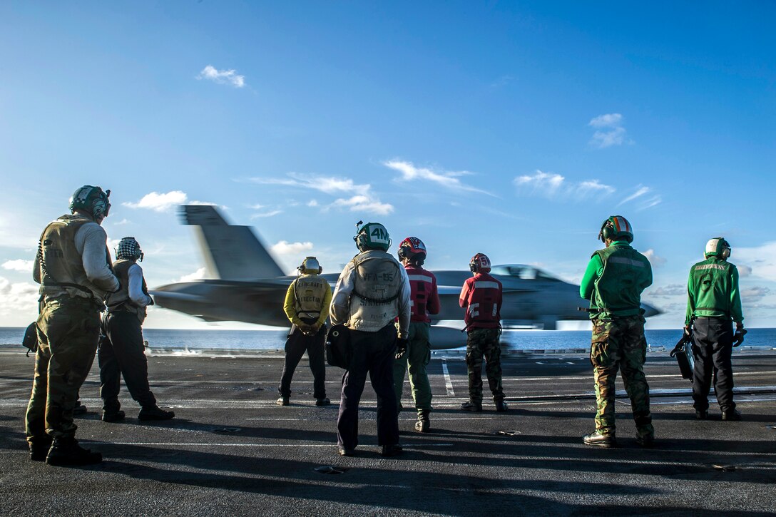 U.S. sailors watch as an F/A-18E Super Hornet from Strike Fighter Squadron 27 launches from the flight deck of the aircraft carrier USS George Washington in the Pacific Ocean, Oct. 17, 2014.