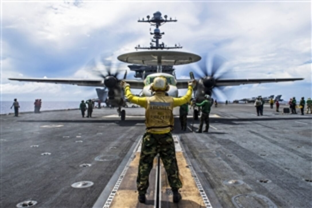 U.S. Navy Petty Officer 3rd Class Blake Danz signals the pilot of an E-2C Hawkeye on the flight deck of the  aircraft carrier USS George Washington in the waters near Guam, Oct. 27, 2014. The George Washington and its embarked air wing, Carrier Air Wing 5, provide a combat-ready force that protects and defends the collective maritime interests of the U.S. and its allies and partners in the Indo-Asia-Pacific region. 