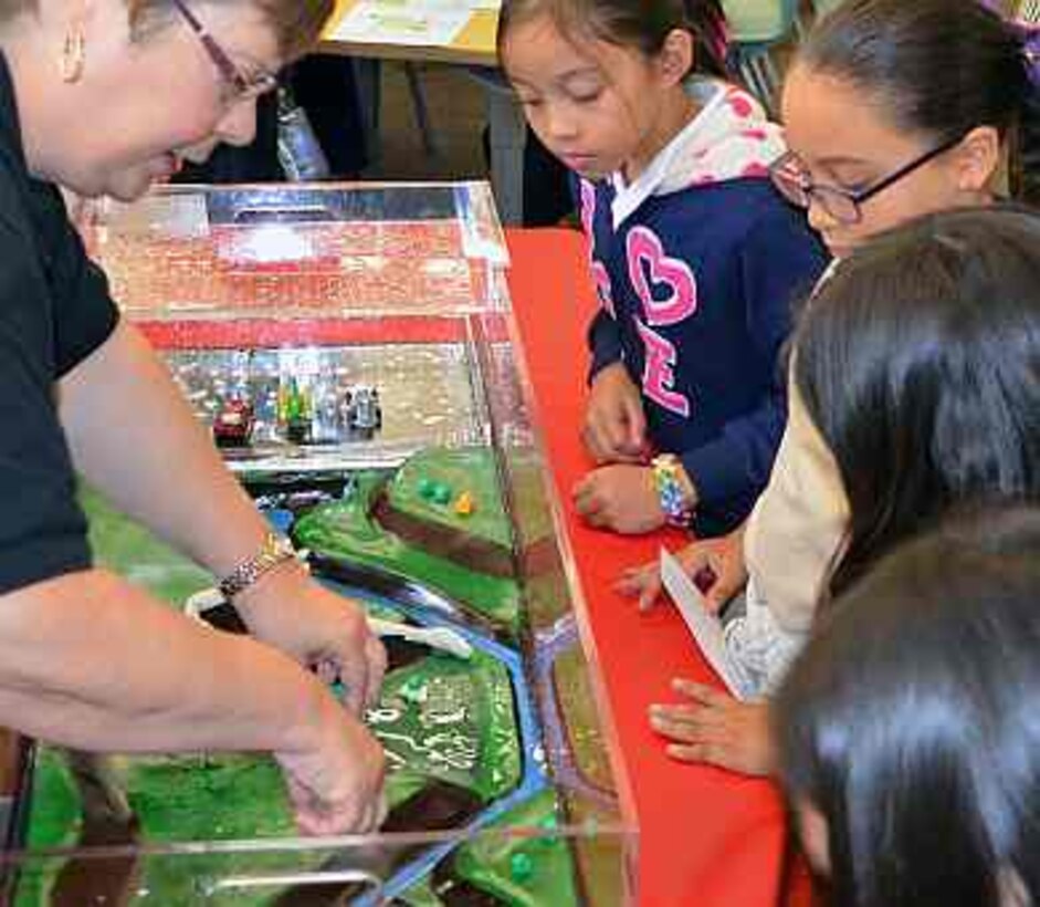 Judy Soutiere, district flood risk manager for the U.S. Army Corps of Engineers Sacramento District, demonstrates how heavy rains can lead to floods that reshape the face of a community. Looking on are students at Westmore Oaks Elementary School in West Sacramento, California, during a California Flood Preparedness Week program event Oct. 21, 2014. Major Jeff Palazzini, deputy district commander, shares flood preparedness tips in this video report.
