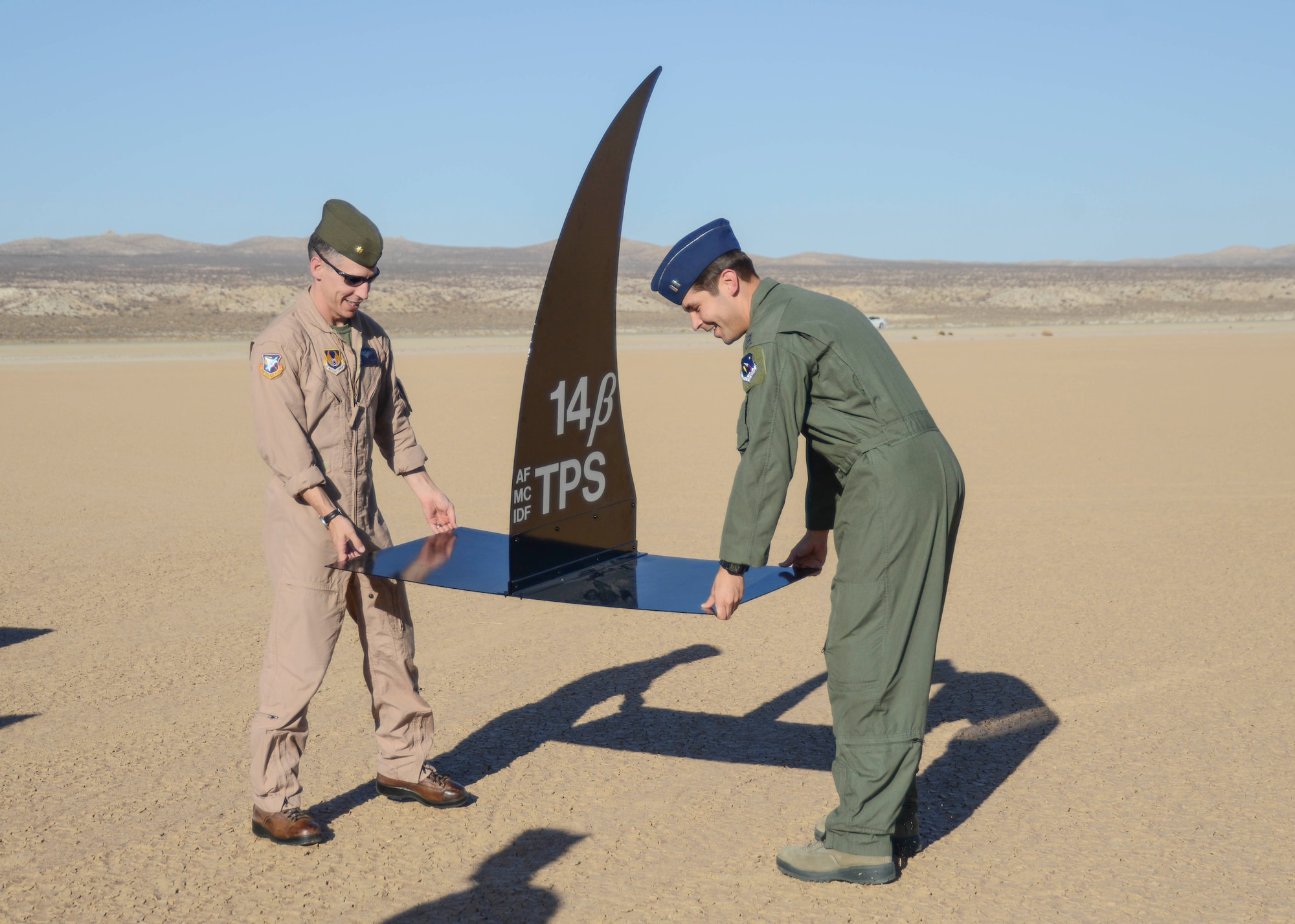 Test Pilot School 14B class leader, Maj. Christopher Allain (left), U.S. Marine Corps, and his fellow student Capt. James McDonald, combat systems officer, place the shark fin on Rosamond Dry Lakebed Oct. 24. (U.S. Air Force photo by Rebecca Amber)
