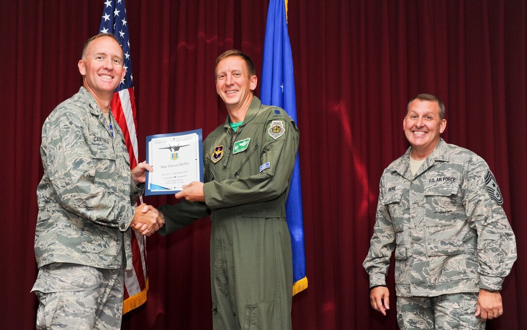 Lt. Col. Eric Smith, 33rd Operation Support Squadron commander, accepts the 33rd FW field grade officer of the quarter award on behalf of Maj. Trevor Hollis, 33rd OSS senior intel officer, from Col. Todd Canterbury, 33rd FW commander, and Chief Master Sgt. Scott Berge, 33rd FW command chief, on Eglin Air Force Base, Fla., Oct 17, 2014. Hollis stood up the first and only F-35 intelligence formal training unit. By driving 386 training hours, two beta classes and graduating 16 students, Hollis’s actions have pioneered the next 40 years of F-35 intelligence support. (U.S. Air Force photo/Staff Sgt. Marleah Robertson)
