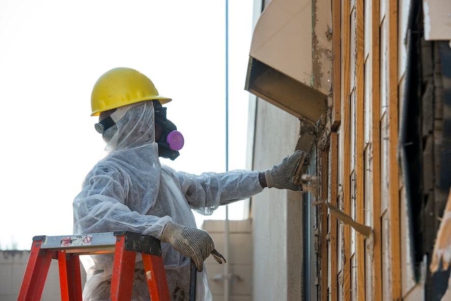 A construction worker removes siding from a building being demolished Oct. 28, 2014, at Moody Air Force Base, Ga. Workers wear masks to protect themselves from inhalation hazards associated with asbestos. (U.S. Air Force photo by Airman 1st Class Ryan Callaghan/Released)