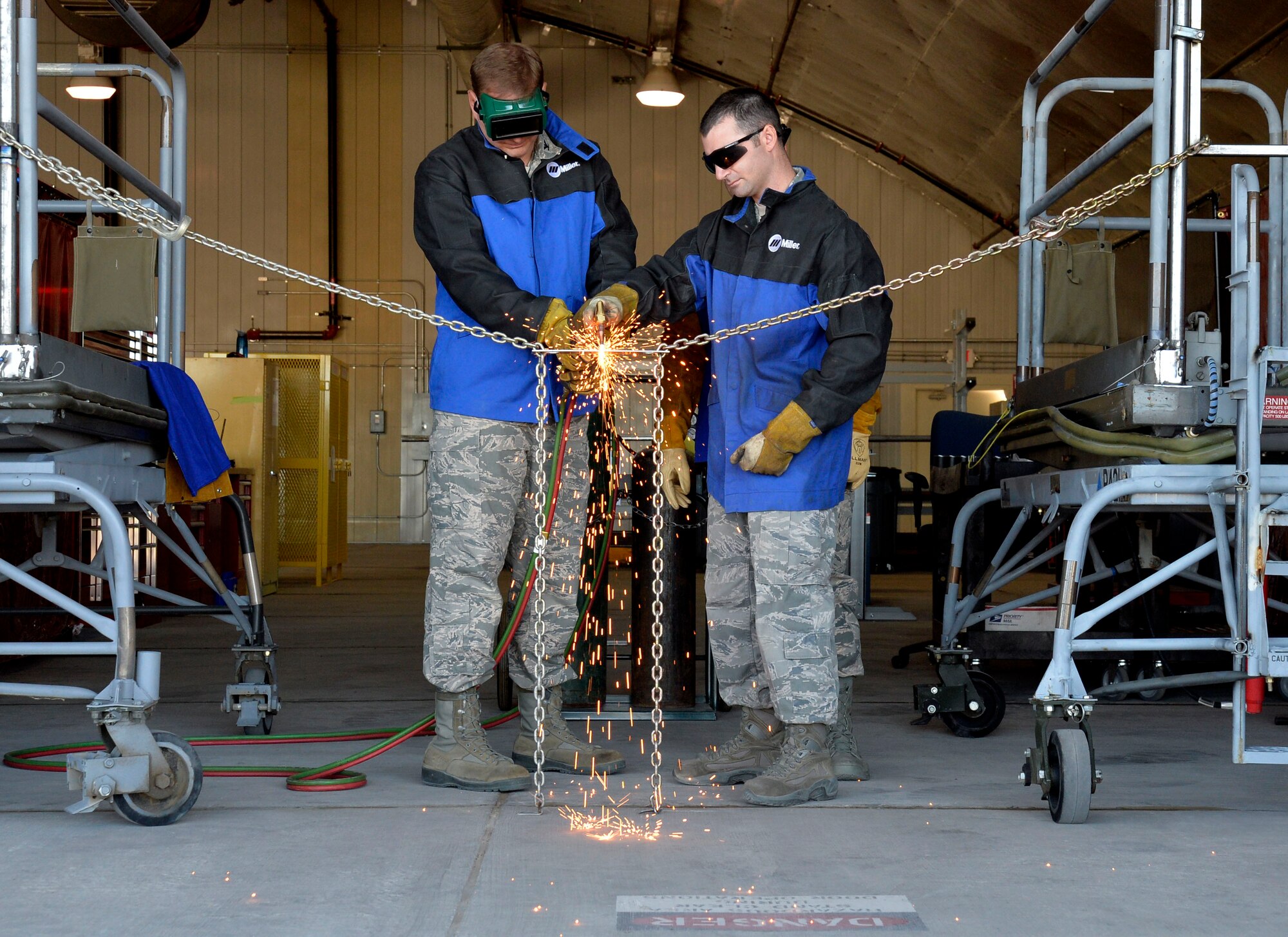 Col. James Chittenden, 432nd Wing/432nd Air Expeditionary Wing vice commander, left, and Staff Sgt. Zachary Arbuckle, 432nd Maintenance Squadron Aircraft Metals Technology Section chief, cut through a metal chain during a “ribbon” cutting ceremony Oct. 9, 2014, at Creech Air Force Base, Nevada. The new facility is the first of its kind here and came to fruition through the cooperative efforts of several units at Creech and Nellis Air Force Bases. (U.S. Air Force photo by Staff Sgt. Adawn Kelsey/released)