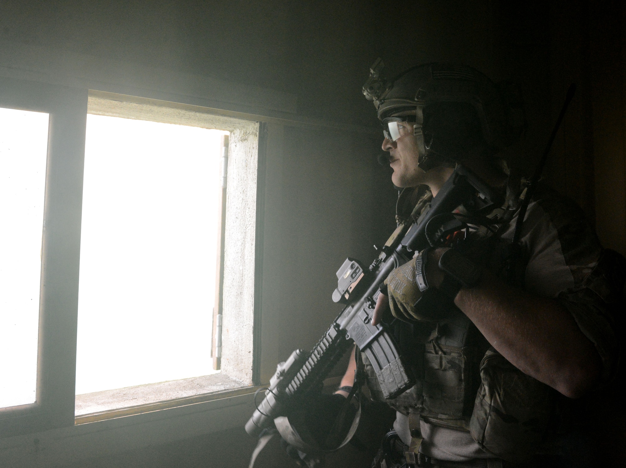 A U.S. Air Force combat controller guards a window in a simulated village under attack during a training exercise Oct. 7, 2014, at Stanford Training Area near Thetford, England. Combat controllers call in air combat power while operating with special operations forces in austere combat environments. The exercise was designed to familiarize special tactics Airmen with combat scenarios preparing for real-world incidents. (U.S. Air Force photo/Senior Airman Kate Maurer/Released)