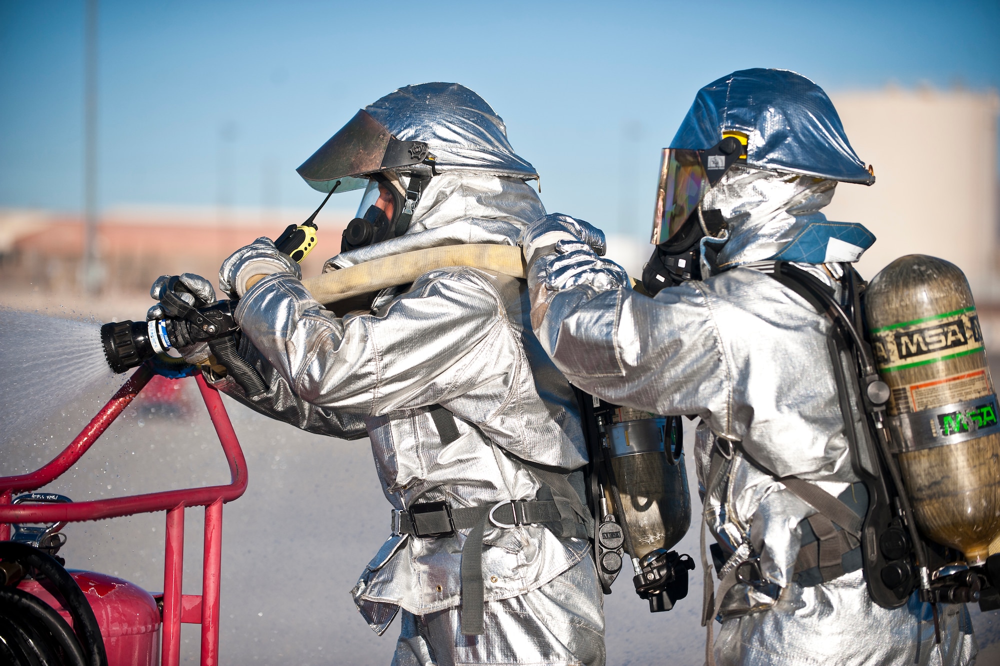 Firefighters from the 99th Civil Engineer Squadron turn on a fire hose at the scene of a simulated aircraft crash site during a major accident response exercise at Nellis Air Force Base, Nev., Oct. 28, 2014. The firefighters put out a simulated fire on an F-16 Fighting Falcon that was playing the role of a downed F-35A Lightning II. (U.S. Air Force photo by Staff Sgt. Siuta B. Ika)