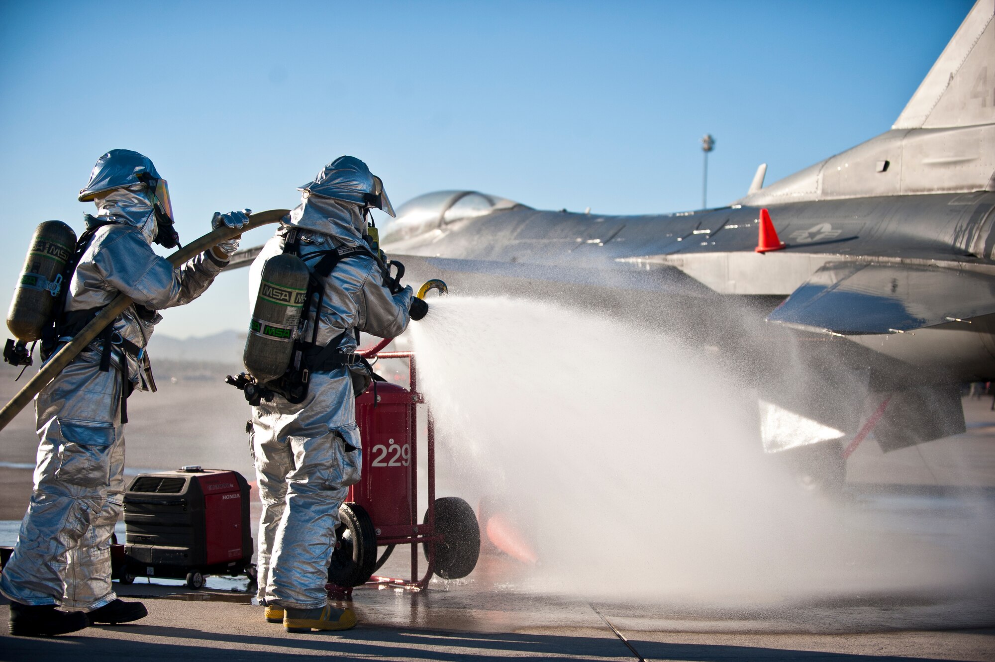 Firefighters from the 99th Civil Engineer Squadron spray an F-16 Fighting Falcon that is playing the role of a downed F-35A Lightning II during a major accident response exercise at Nellis Air Force Base, Nev., Oct. 28, 2014. The firefighters were evaluated on how quickly and safely they could put out a simulated fire on the aircraft. (U.S. Air Force photo by Staff Sgt. Siuta B. Ika)