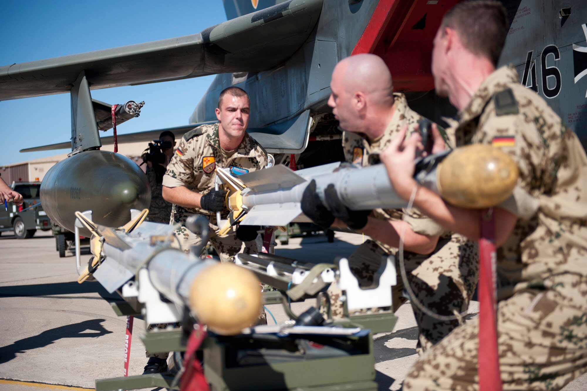 Tech. Sgt. Andre Wells, Staff Sgt. Felix Urban and Senior Airman Marcus Schiller, all German Air Force Flying Training Center crew chiefs, prepare an inert missile for a Tornado jet during a quarterly load crew competition at Holloman Air Force Base, N.M., Oct. 24. The GAF load crew participated in the competition to have their skills evaluated alongside the F-16 Fighting Falcon and MQ-9 Reaper load crews. For the competition, points are awarded for weapons-loading, toolkit inspection, and uniform inspection.  (U.S. Air Force photo by Senior Airman Daniel Liddicoet/Released)