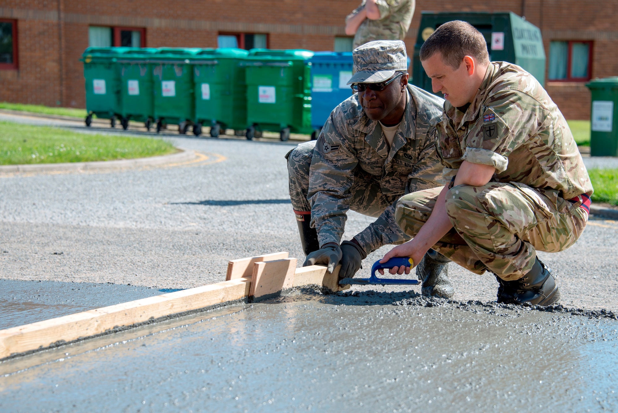 U.S. Air Force Airman 1st Class Brice Gadjoro, 140th Civil Engineer Squadron, Colorado Air National Guard, and British Army Lance Cpl. James Shannon, 39 Engineer Regiment, use a wood beam to smooth out the top of freshly laid cement that will help improve the base junior dorms area once completed, during a deployed for training trip, known as Exercise Flying Rose at Kinloss Barrack in Forres, Moray, Scotland, United Kingdom, Jun. 16, 2014. Over 40 members of the 140th CES are in Scotland for their annual training and are accomplishing five construction projects that will improve several areas around Kinloss Barracks, during Exercise Flying Rose hosted by the British Army before returning back to Colorado later this month. (U.S. Air National Guard photo by Tech. Sgt. Wolfram M. Stumpf)