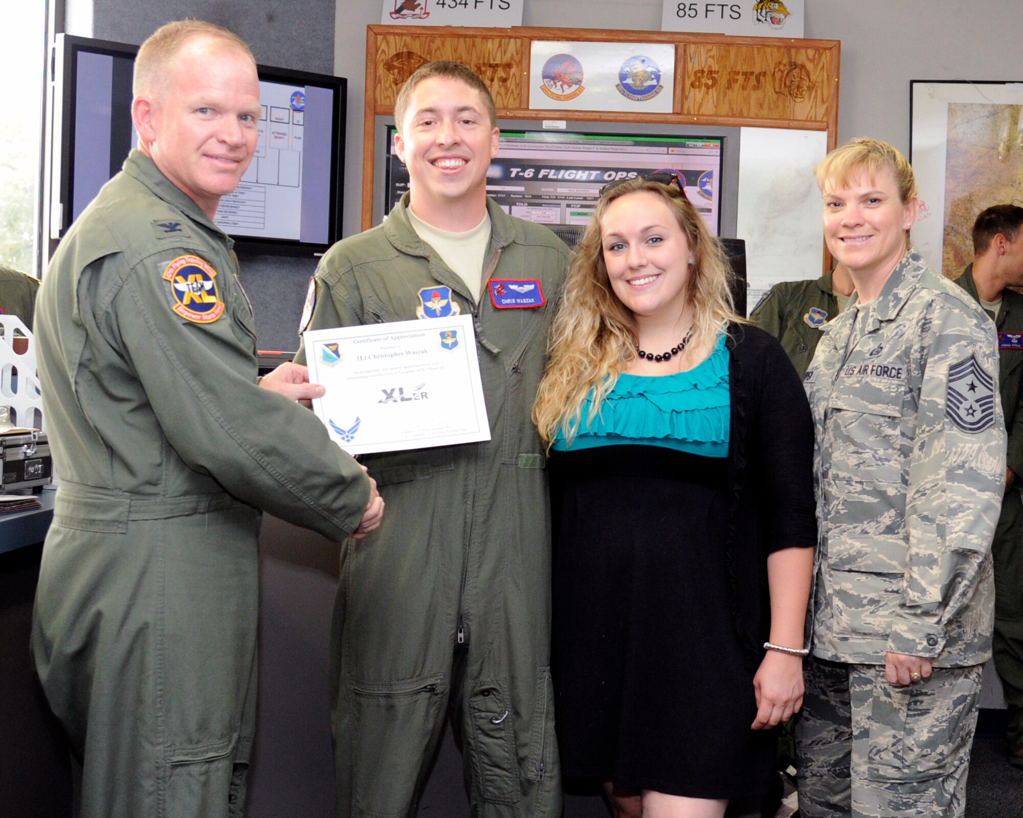 First Lieutenant Christopher Waszak, center-left, 434th Flying Training Squadron T-6A Texan II instructor pilot, and Danielle Waszak, center-right, pose with Col. Darrell Judy, left, 47th Flying Training Wing vice commander, and Chief Master Sgt. Teresa Clapper, right, 47th FTW command chief, after being presented the XLer of the week award here Oct. 29, 2014. The XLer is a weekly award chosen by wing leadership and is presented to those who consistently make outstanding contributions to their unit and Laughlin. (U.S. Air Force photo by Airman 1st Class Jimmie D. Pike)(Released)