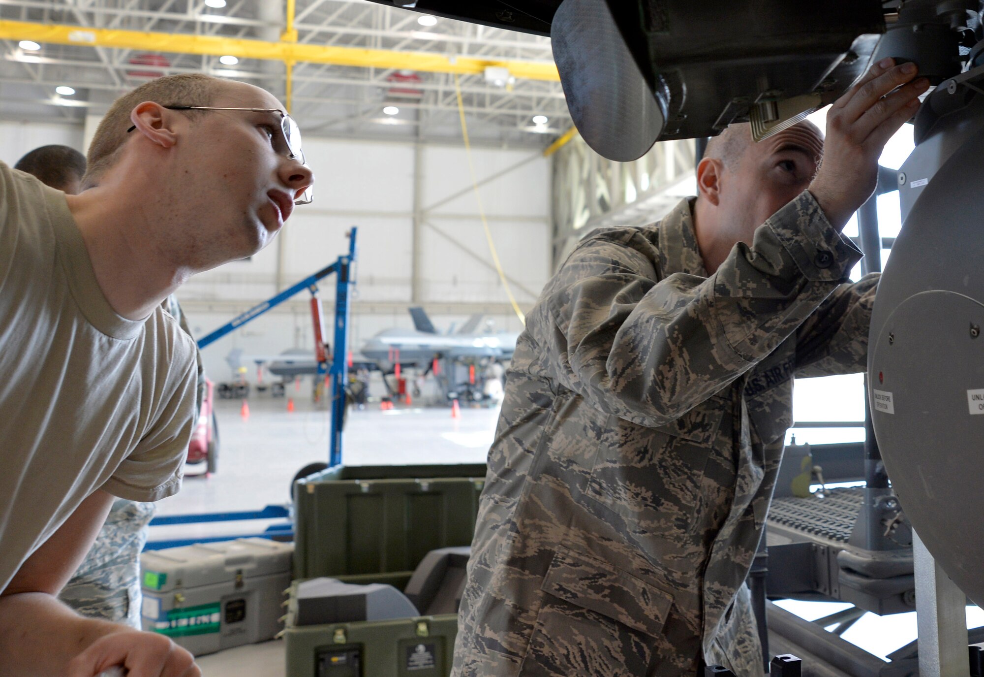Senior Airman William Little, 727th Special Operations Aircraft Maintenance Squadron avionics specialist from Cannon Air Force Base, New Mexico, left, observes as Lt. Col. Scott, 11th Reconnaissance Squadron director of operations, checks the placement of the Multi-spectral Targeting System ball on an MQ-9 Reaper during integration training Oct. 22, 2014, at Creech AFB, Nevada. The integration training program was developed to help foster the relationship between the maintenance and operations squadrons on base. (U.S. Air Force photo by Staff Sgt. Adawn Kelsey/released some names have been withheld for security purposes)