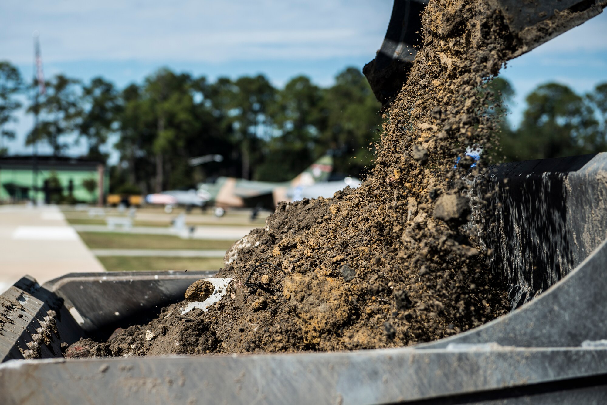 Dirt falls from an excavator bucket into a front-end loader bucket Oct. 29, 2014, at Moody Air Force Base, Ga. To safely house an HC-130P Combat King, the 23d Civil Engineer Squadron added concrete, weight-bearing pads to the President George W. Bush Air Park. (U.S. Air Force photo by Airman 1st Class Ryan Callaghan/Released)