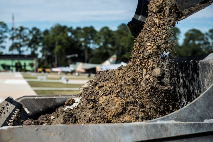 Dirt falls from an excavator bucket into a front-end loader bucket Oct. 29, 2014, at Moody Air Force Base, Ga. To safely house an HC-130P Combat King, the 23d Civil Engineer Squadron added concrete, weight-bearing pads to the President George W. Bush Air Park. (U.S. Air Force photo by Airman 1st Class Ryan Callaghan/Released)
