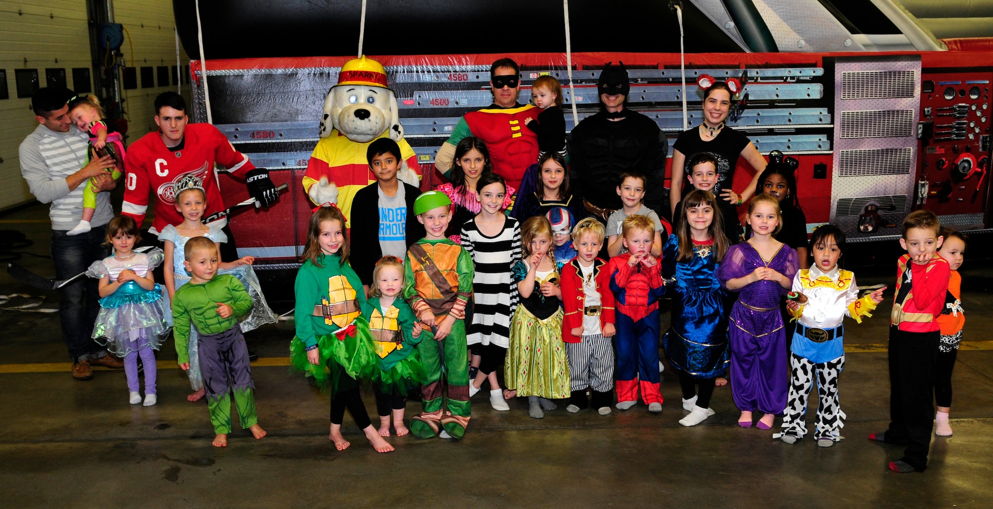 Team Mildenhall children and volunteers pose for a photo during the Hearts Apart event at the fire department Oct. 29, 2014, on RAF Mildenhall, England. Firefighters decorated the fire station with a Halloween theme as children walked around the station collecting candy. The monthly event for families of deployed members is hosted by various units around base in conjunction with the Airman and Family Readiness Center. (U.S. Air Force photo by Karen Abeyasekere/Released)
