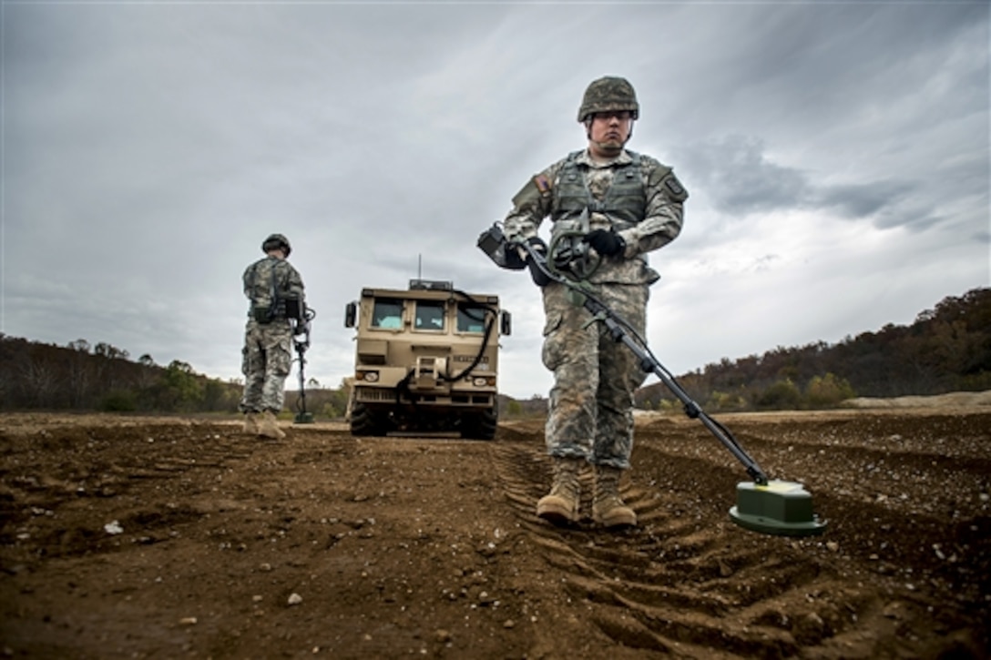 Army Pvt. Ronnie Gallegos, right, and Pfc. Judge Parker, left, use hand-held mine detectors to sweep a path up to the M1271 mine-clearing vehicle during the extraction and recovery portion of a weeklong team-oriented course held on Fort Leonard Wood, Mo., Oct. 30, 2014. 