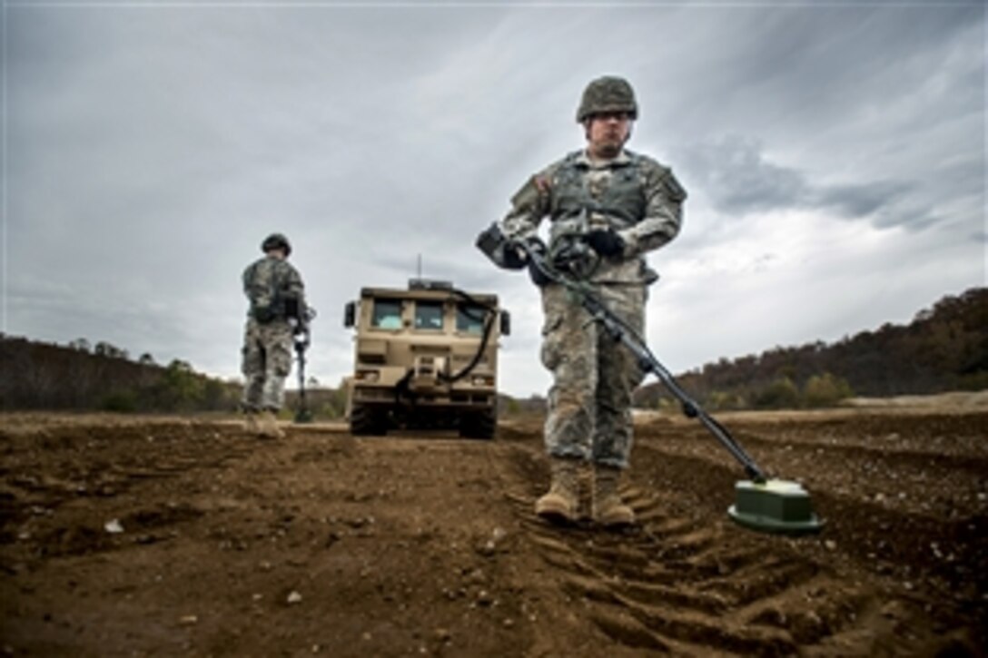 Army Pvt. Ronnie Gallegos, right, and Pfc. Judge Parker, left, use hand-held mine detectors to sweep a path up to the M1271 mine-clearing vehicle during the extraction and recovery portion of a weeklong team-oriented course held on Fort Leonard Wood, Mo., Oct. 30,2014. 