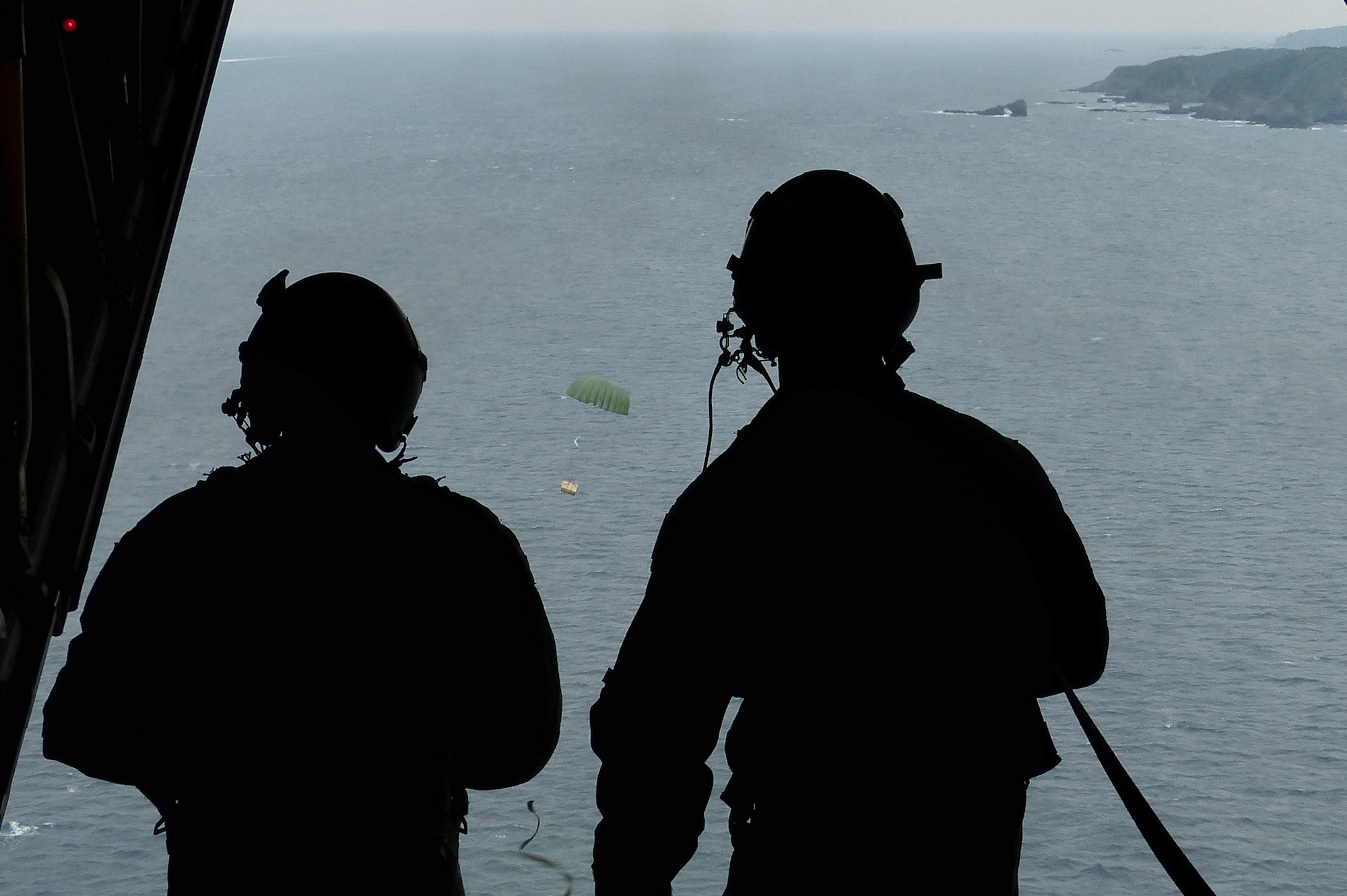 Airman 1st Class Dillon Howell, left, and Staff Sgt. Napoleon Ortiz, loadmasters assigned to the 36th Airlift Squadron, Yokota Air Base, Japan, watch a low-cost, low-altitude airdrop bundle hit its target during a bilateral disaster relief exercise supporting Shizuoka Prefecture Government Aug. 31, 2014. The LCLA bundle contained 300 pounds of rice and water that was retrieved by Japanese fishermen. Airmen from the 374th Airlift Wing participated in three disaster management exercises with Japanese first responders and an additional joint exercise with Marine counterparts Aug. 30 and 31. (U.S. Air Force photo by 1st Lt. Jake Bailey/Released)