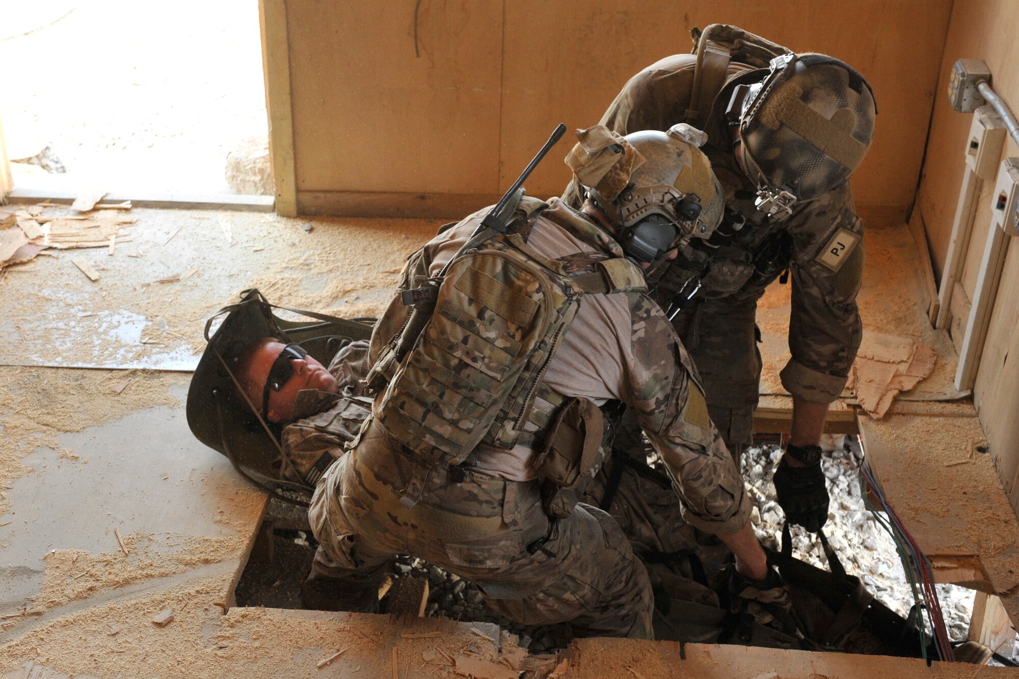 U.S. Air Force pararescuemen from the 83rd Expeditionary Rescue Squadron move mock patient, Airman 1st Class Benjamin Martin, out through a hole in the floor during a mission rehearsal in an excess structure here Aug. 26, 2014. The event allowed PJs to hone their breaching, clearing, patient care and egress skills. Air Force rescue forces conduct combat search and rescue and personnel recovery operations. The Airmen are deployed from Davis-Monthan Air Force Base, Ariz. Martin is a native of Colorado Springs, Colo. The 83rd ERQS partnered with Joint Task Force Trailblazer, U.S. Army 2nd Engineer Brigade, to use the structure prior to its scheduled deconstruction. Task Force Trailblazer is currently demolishing 50-70 wooden structures here each week as part of Operation Enduring Freedom retrograde operations. (U.S. Air Force photo by Maj. Brandon Lingle/Released)