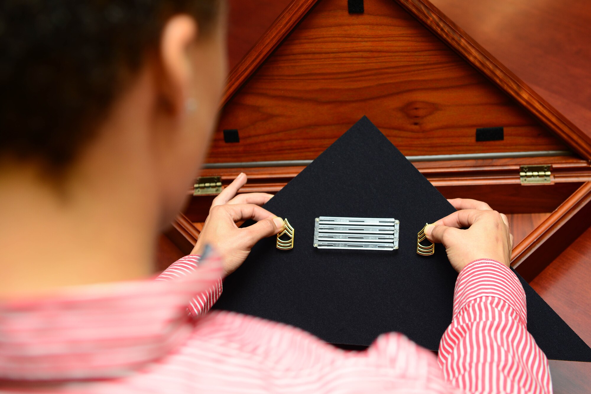 Amber Hendricks, Army Support Activity mortuary affairs coordinator, places a ribbon rack and rank inside of a flag case at Fort Eustis, Va., Aug. 26, 2014. Hendricks creates the cases for family members of the deceased U.S. Army Soldier. (U.S. Air Force photo by Airman 1st Class Kimberly Nagle/Released) 