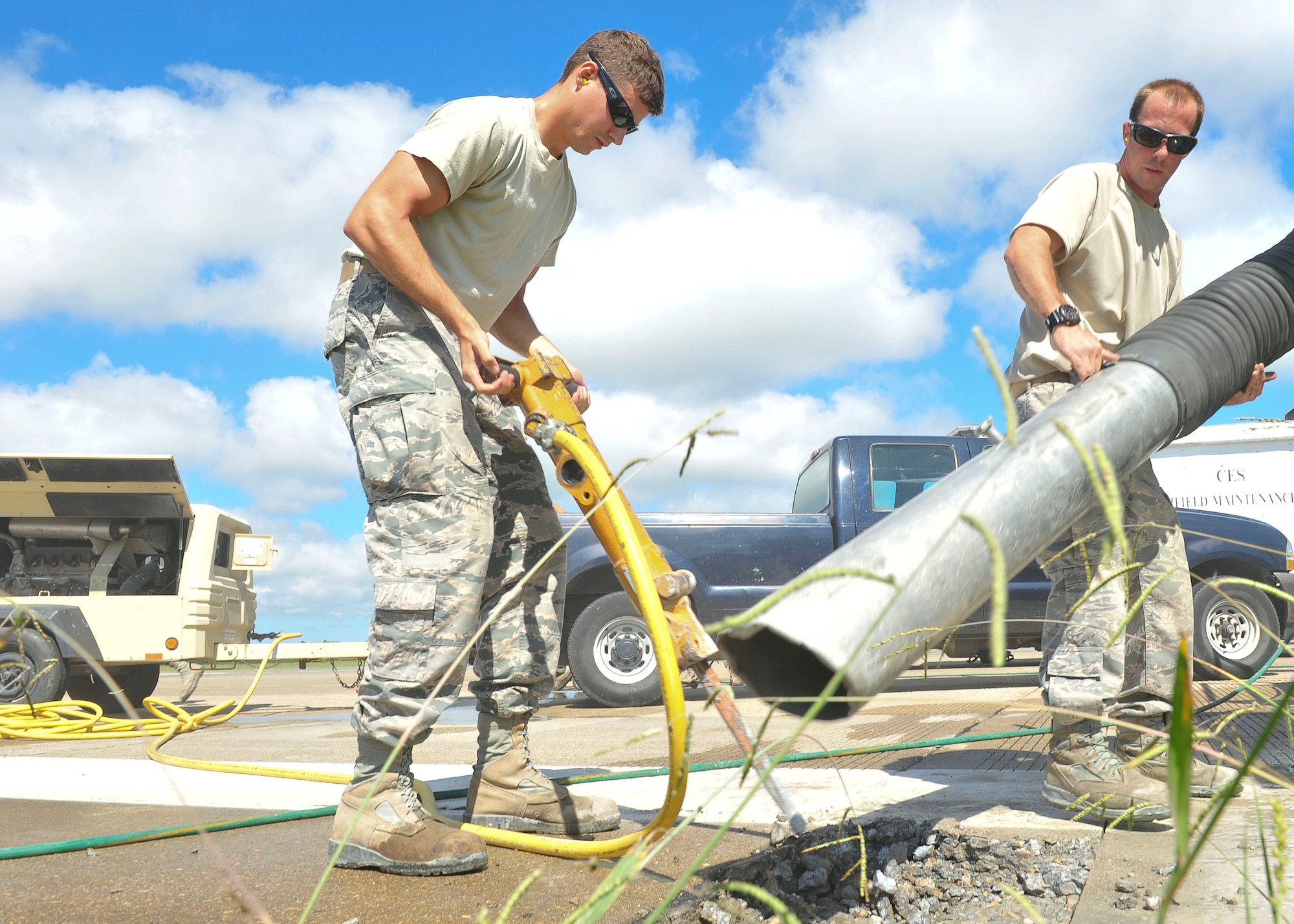 U.S. Air Force Senior Airman Daniel Konik and Staff Sgt. Christopher Duerr, 633rd Civil Engineer Squadron pavements and equipment craftsmen, use a jack-hammer and a vacuum hose from a sweeper truck to repair sections of the runway at Langley Air Force Base, Va., Aug. 27, 2014.  The 633rd CES pavements and equipment Airmen repaired a cracked portion of the runway and to help prevent foreign object damage to aircraft. (U.S. Air Force photo by Senior Airman Connor Estes/Released)