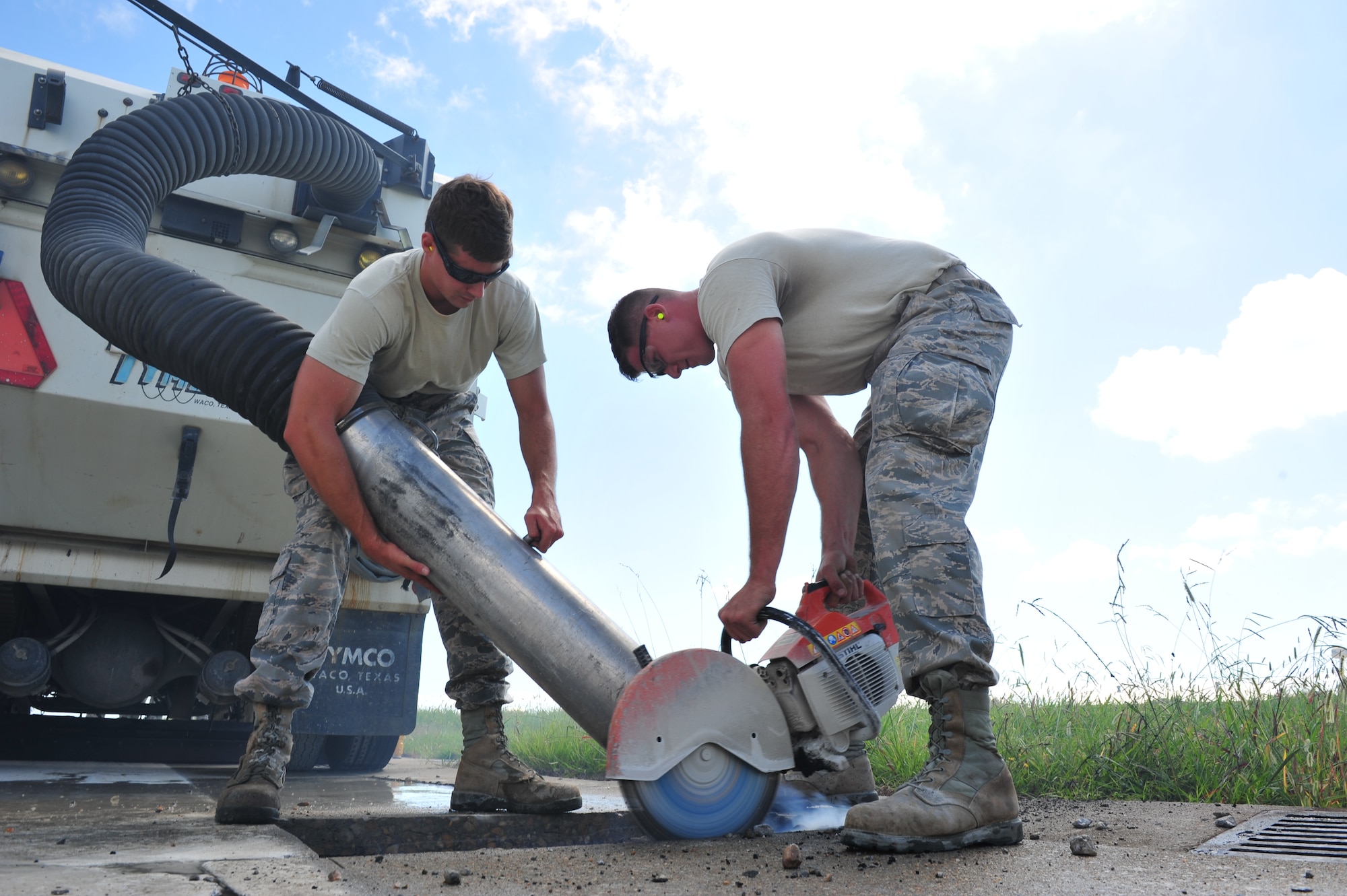 U.S. Air Force Senior Airmen Daniel Konik and Jordan Noonan, 633rd Civil Engineer Squadron pavements and equipment craftsmen, cuts a section of the runway and a sweeper truck to vacuum up debris at Langley Air Force Base, Va., Aug. 27, 2014.  The 633rd CES closed the runway to patch damaged areas, ultimately ensuring flight line safety. (U.S. Air Force photo by Senior Airman Connor Estes/Released)