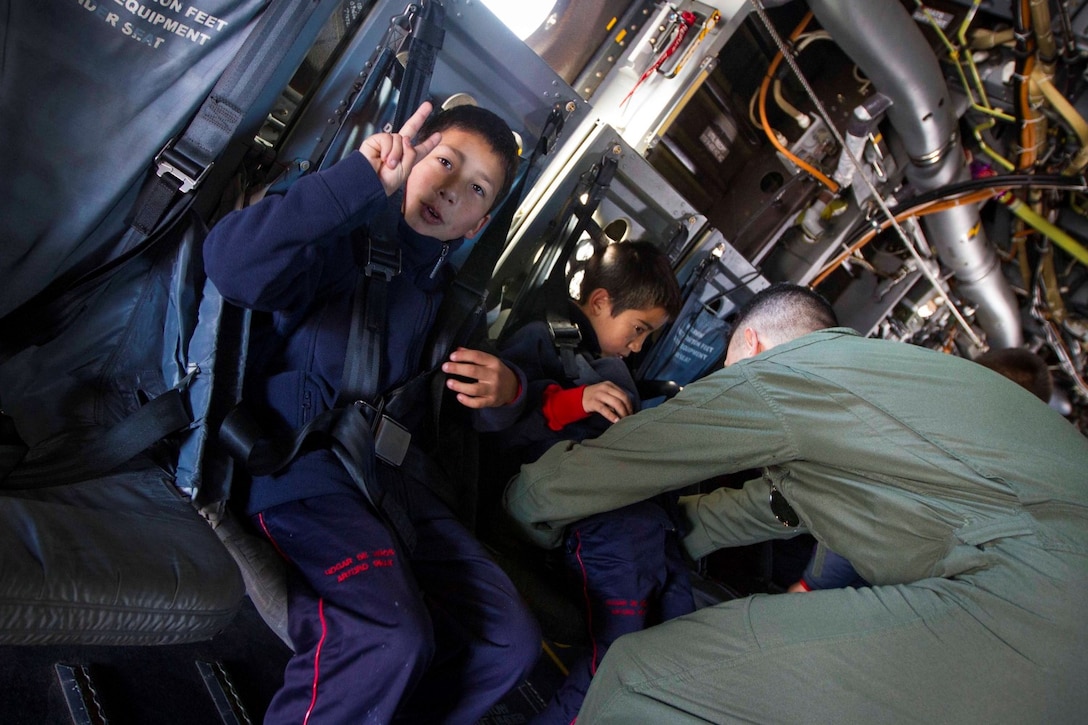 Captain George Cummings, an MV-22 pilot with Marine Operational Test and Evaluation Squadron 22 (VMX-22), straps children from a local school into seats on an MV-22 Osprey during a tour aboard the future amphibious assault ship USS America (LHA 6) in Valparaiso, Chile, Aug. 25, 2014. The children were given the opportunity to get hands on with several static displays hosted by Marines and Sailors showcasing the capabilities that Special Purpose Marine Air Ground Task Force South brings to the ship. SPMAGTF-South is embarked aboard America in support of her maiden transit “America Visits the Americas.” The transit demonstrates the capabilities that the Navy-Marine Corps team brings to our nation and partners. (U.S. Marine Corps photo by Cpl. Donald Holbert/ Released)