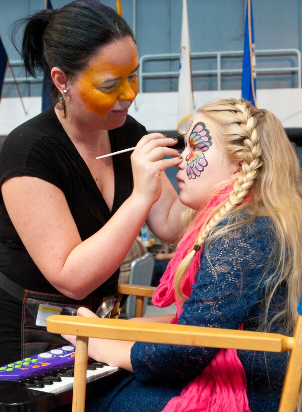 Lindsey Hand, wife of 2nd Lt. Christopher Hand, 321st Missile Squadron deputy missile combat crew commander, paints the face of Alicen Thomas, 9, granddaughter of Navy Chief Petty Officer, retired, Lilian Howard at a flea market in the Fall Hall Community Center Aug. 30, 2014. During the flea market Hand used her face painting skills as opposed to selling items. (U.S. Air Force photo by Airman Malcolm Mayfield)