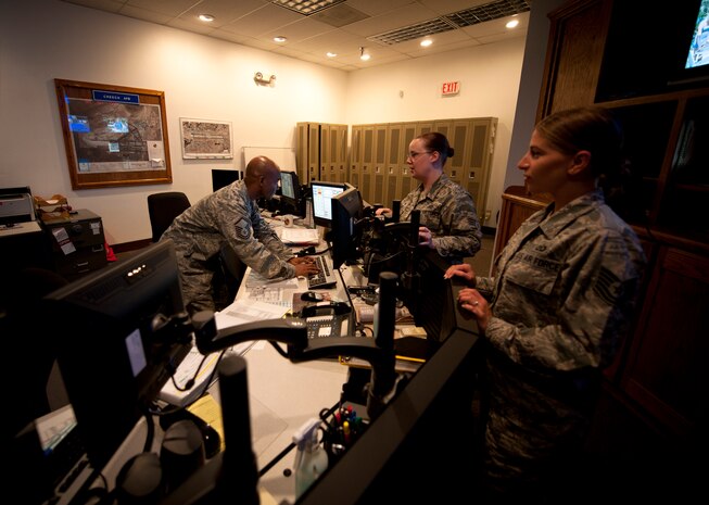 Master Sgt. Jamone Taylor (left), 99th Air Base Wing Command Post NCO in charge of operations, looks over a checklist for Senior Airman Sarah Myers (middle) and Tech. Sgt. Laura Langley, 99th ABW Command Post junior and senior controllers, at Nellis Air Force Base, Nev., Aug. 21, 2014. While most base personnel may only see or hear the controllers work when the ‘giant voice’ goes off or the AtHoc mass notification system pops up with a weather warning, command post personnel are constantly monitoring interactions occurring around the installation. (U.S. Air Force photo by Staff Sgt. Siuta B. Ika)