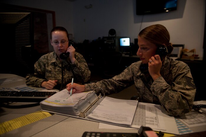 Senior Airman Sarah Myers (left) and Tech. Sgt. Laura Langley, 99th Air Base Wing Command Post junior and senior controllers, make phone calls while running a range fire condition checklist at Nellis Air Force Base, Nev., Aug. 21, 2014. To complete the range fire condition checklist, controllers must call more than 10 different agencies at Nellis and Creech AFBs, as well as the Nevada Test and Training Range to inform personnel of the chances of a wild fire occurring. (U.S. Air Force photo by Staff Sgt. Siuta B. Ika)