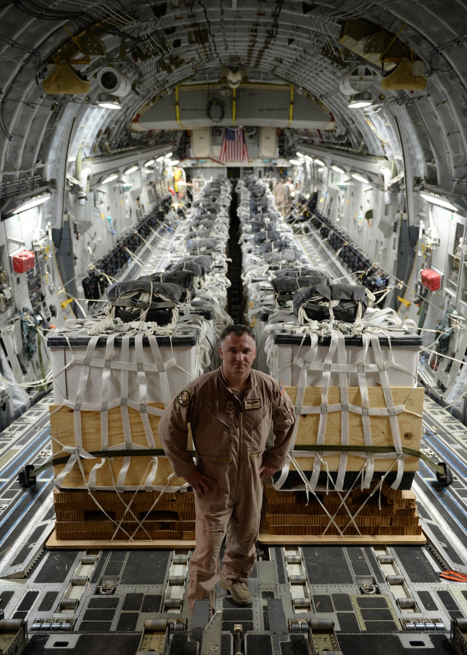 Air Force Master Sgt. Stephen Brown poses in front of 40 container delivery system bundles filled with fresh drinking water on a C-17 Globemaster III in preparation for a humanitarian airdrop over the area of Amirli, Iraq, Aug. 30, 2014. Brown taped candy to most of the bundles in hopes of bringing cheer to displaced Iraqi children. U.S. Air Force photo by Staff Sgt. Shawn Nickel